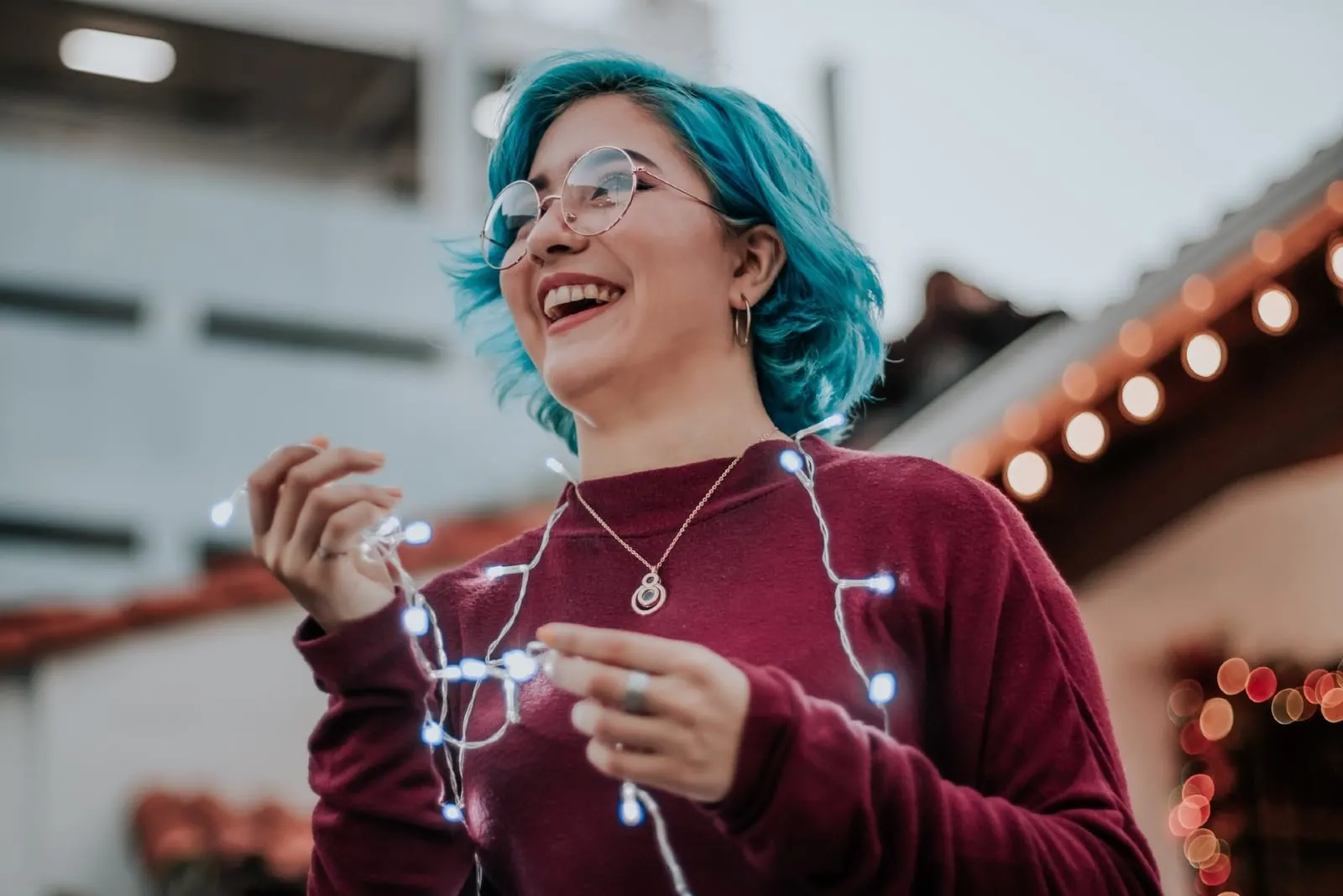 woman with blue hair holding string lights outdoor