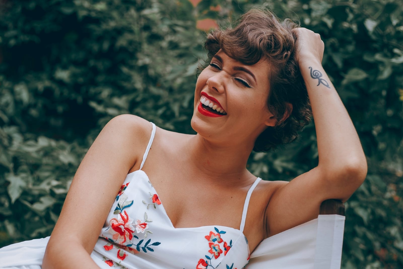 woman with red lipstick laughing while sitting on chair outdoor