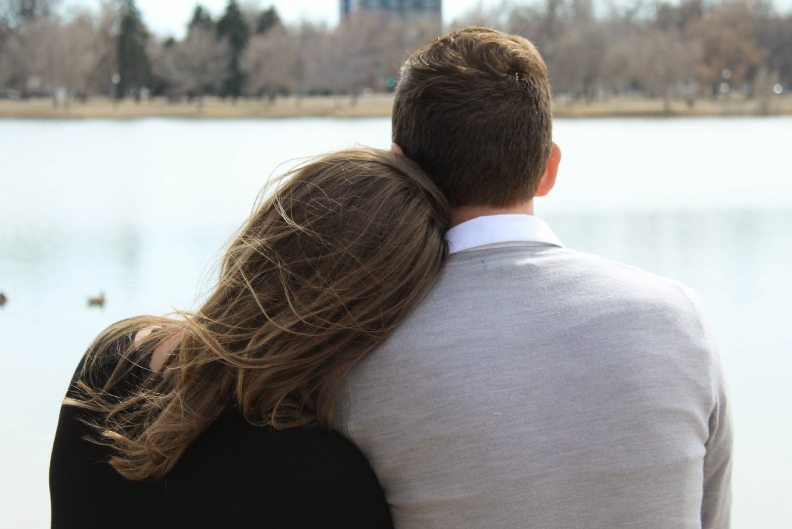 woman leaning on man's shoulder while sitting near water