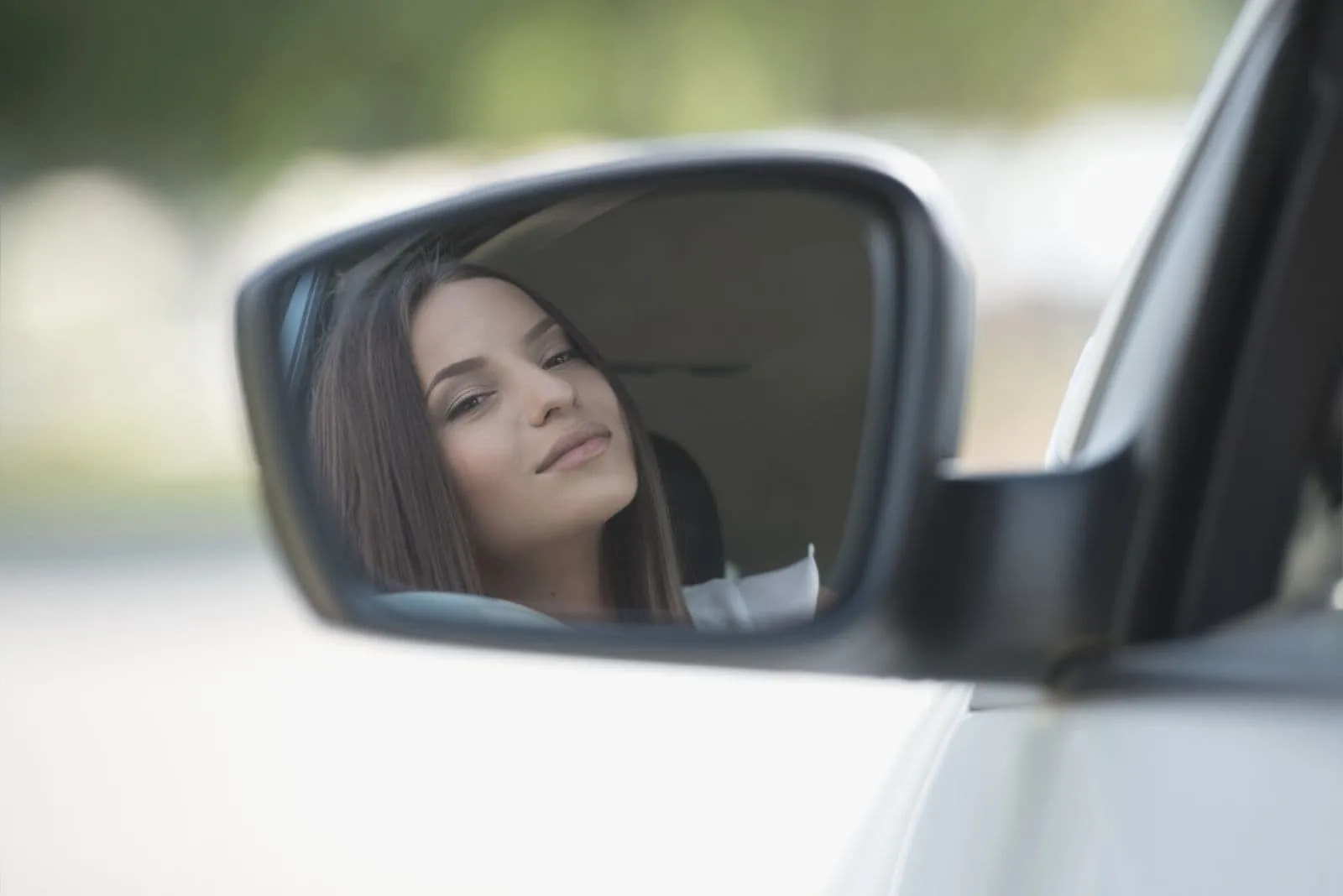 woman looking at herself in the side mirror of her car while driving