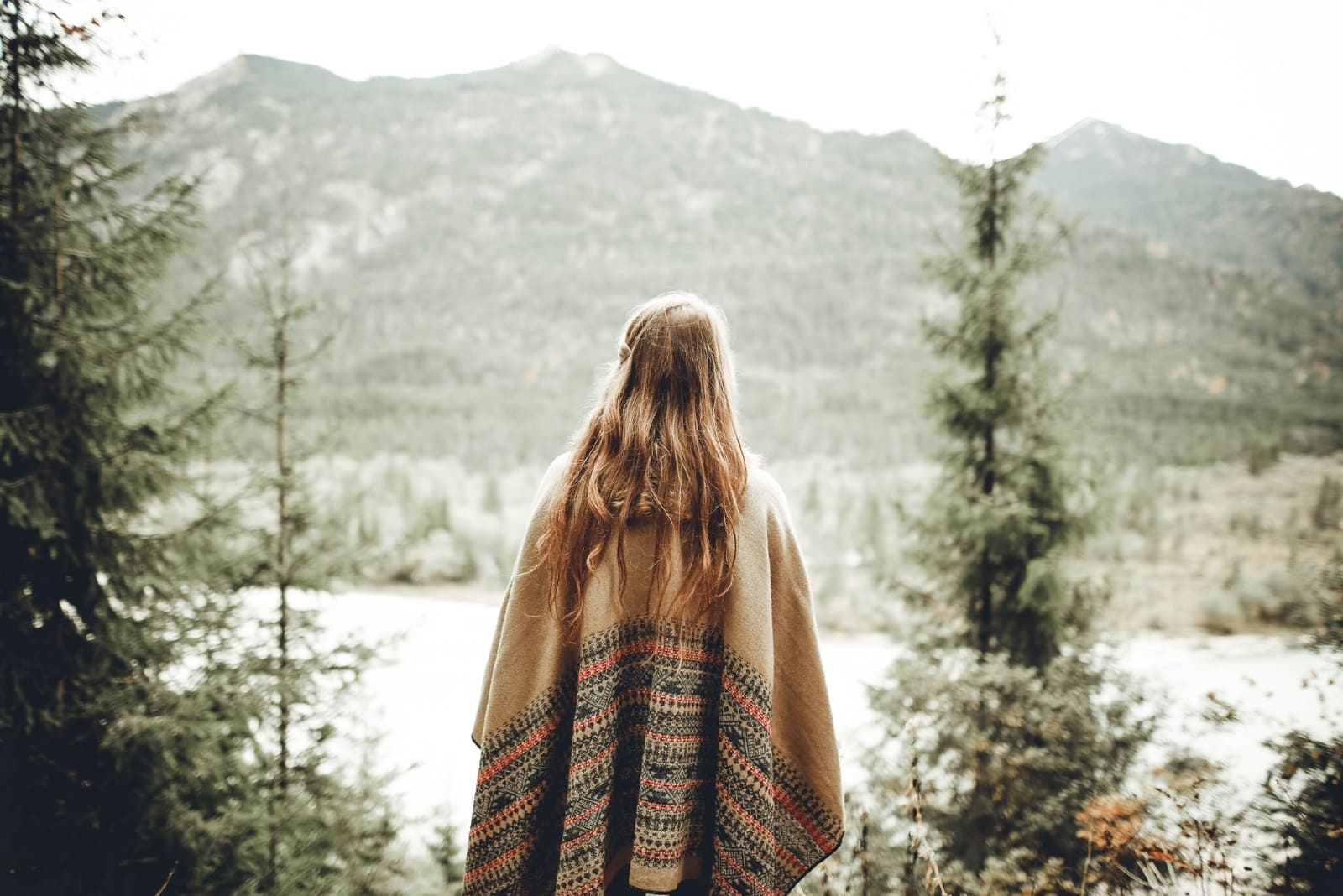 donna con poncho marrone che guarda la montagna