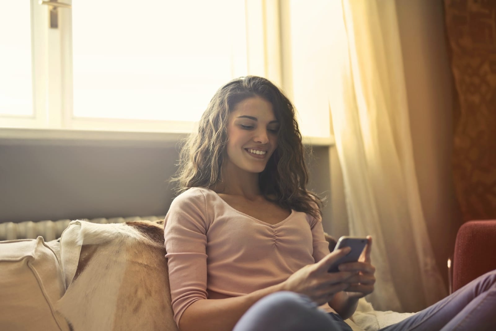 happy woman looking at phone while sitting on bed