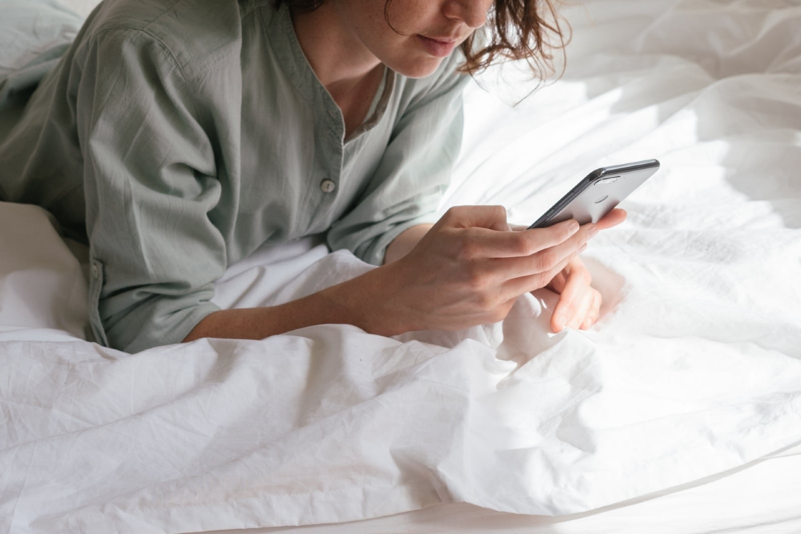 woman looking at phone while laying on bed