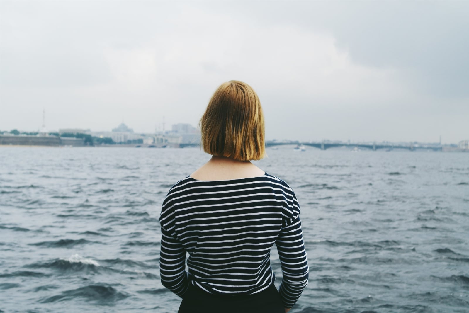 mujer rubia con top de rayas mirando al mar