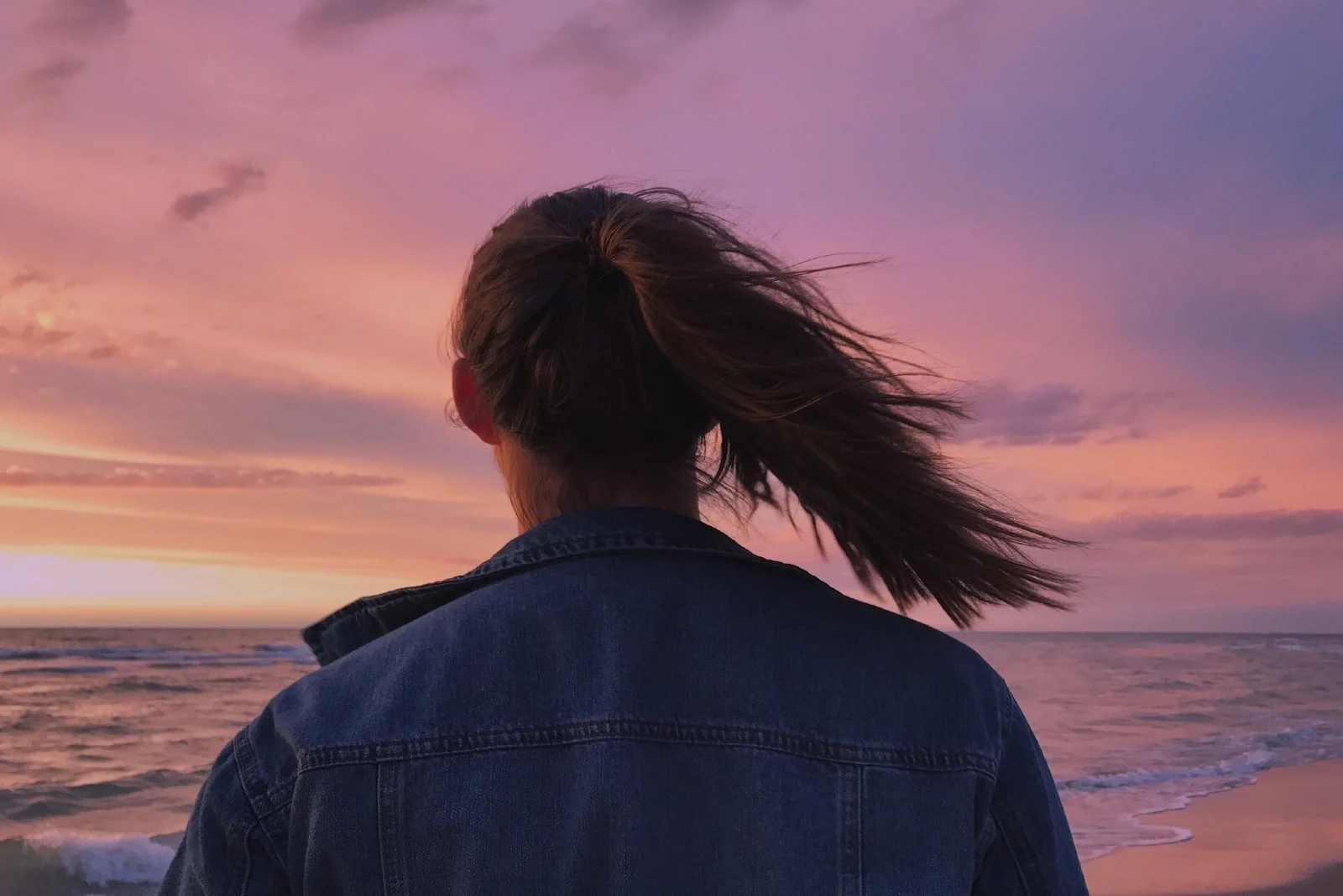 woman in denim jacket looking at sea during sunset