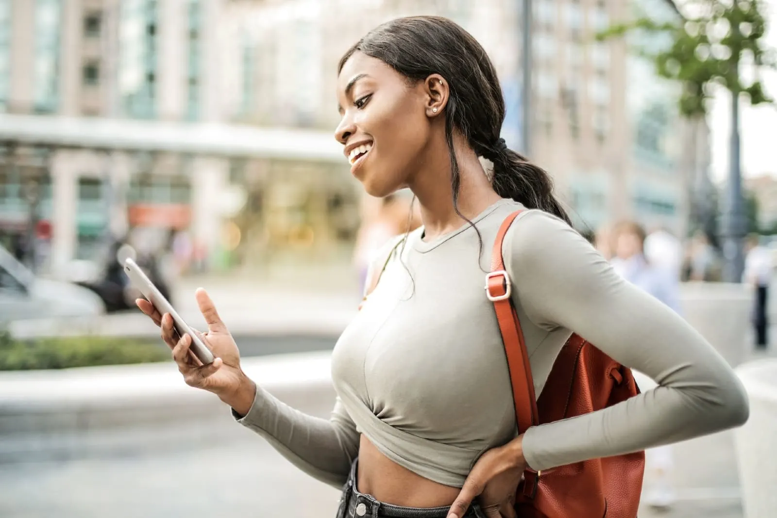 happy woman looking at smartphone while standing on street