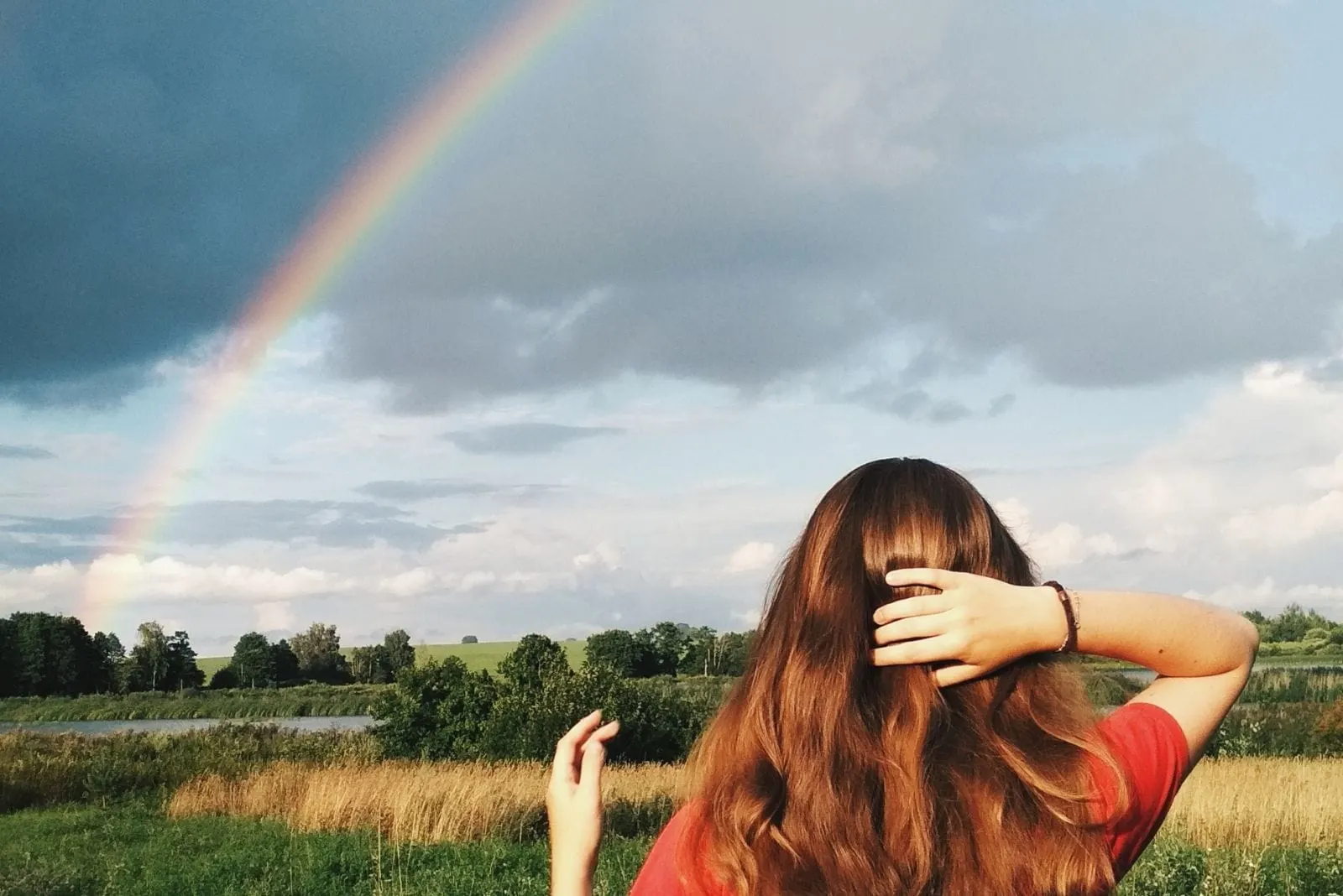 woman looking at the rainbow over the meadows while holding her hair/head