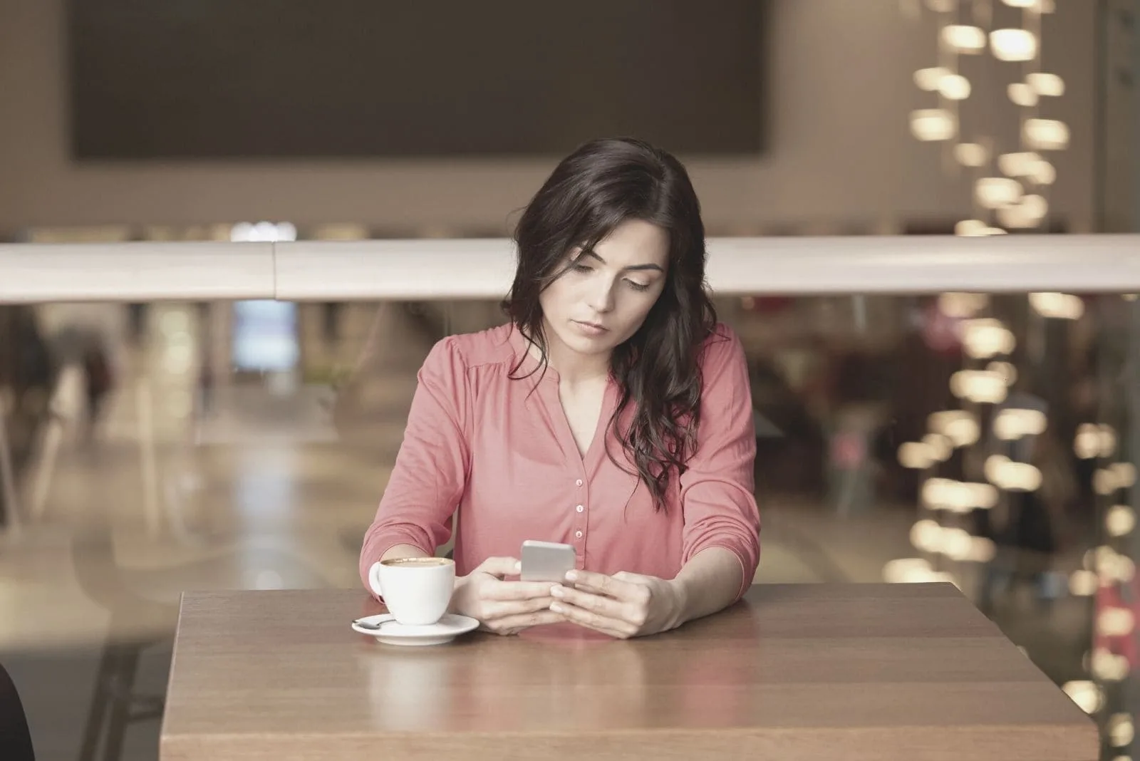 woman looking at the smartphone while having coffee at a cafe