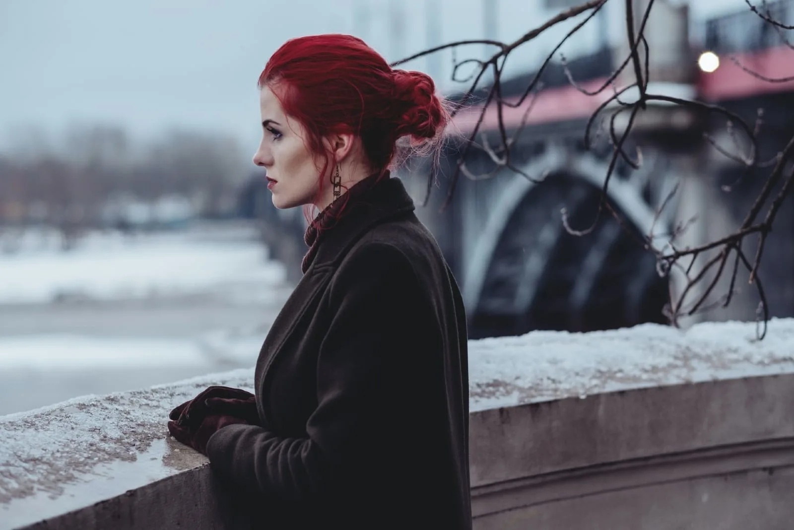 red haired woman in black coat looking at water