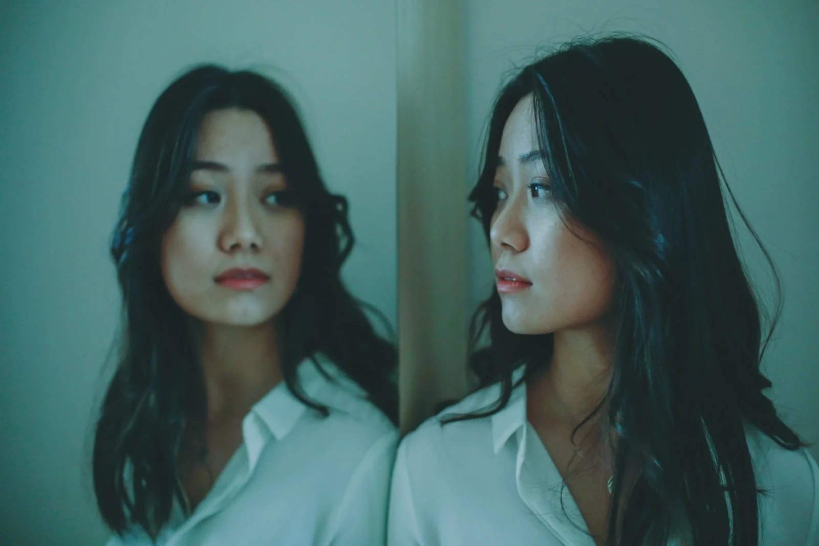 pensive woman in white shirt looking in the mirror