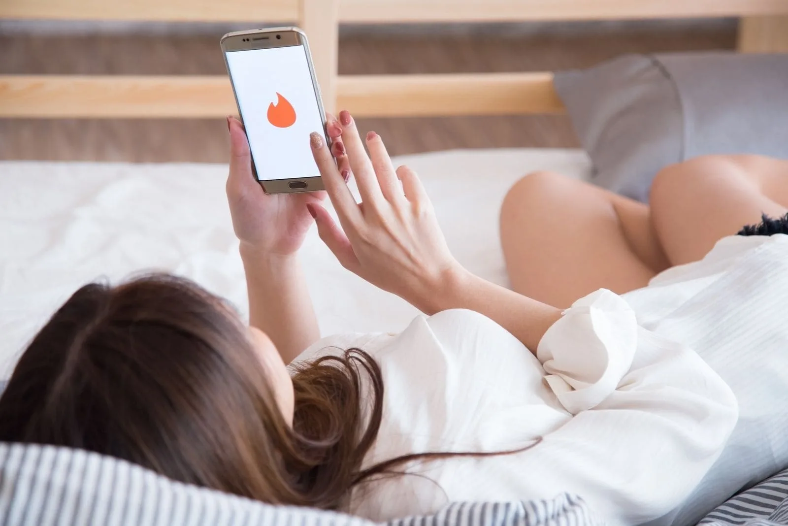 woman opening tinder app while lying down on a bed 