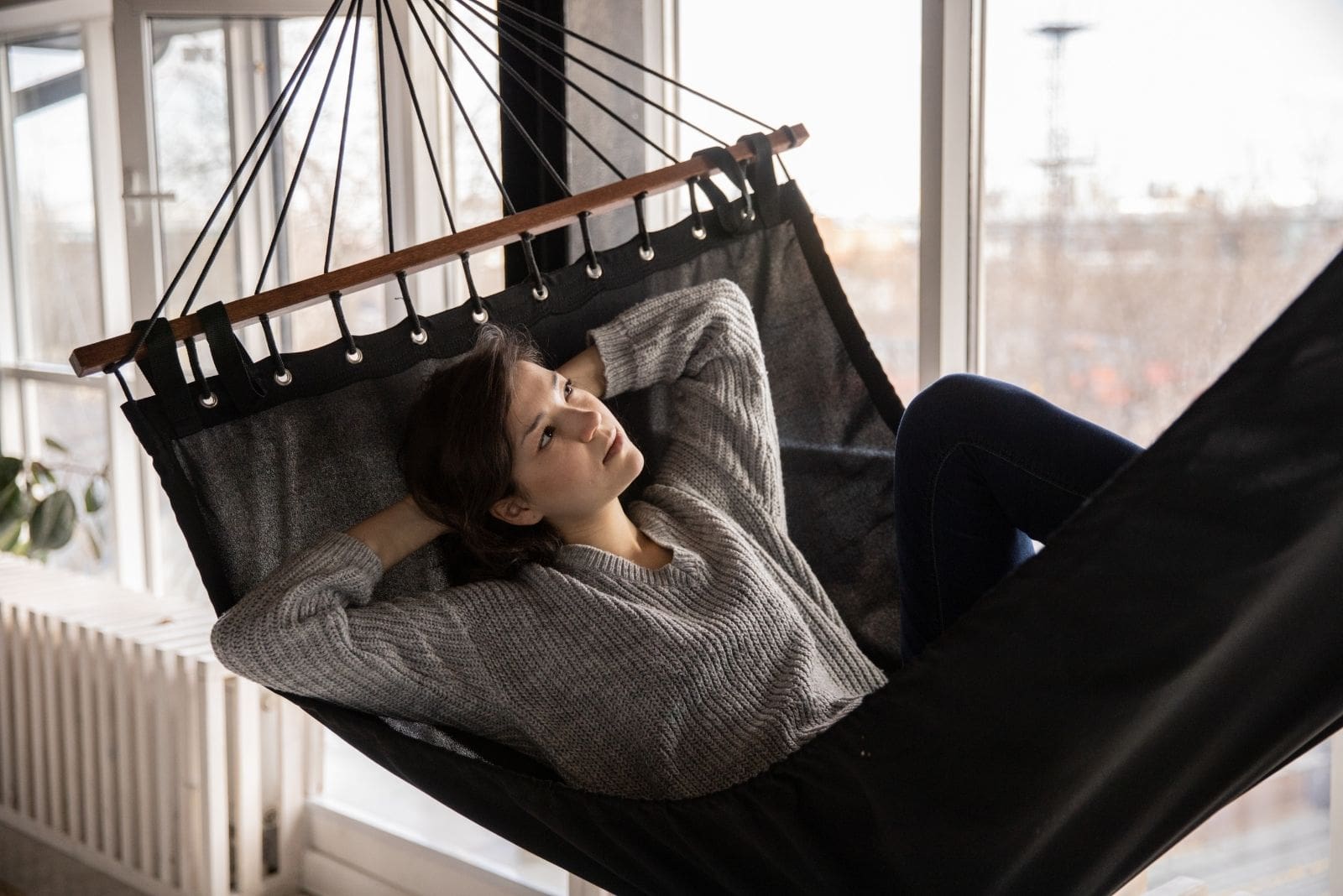 woman relaxing in a hammock inside the house/room building while thinking deeply and relaxing