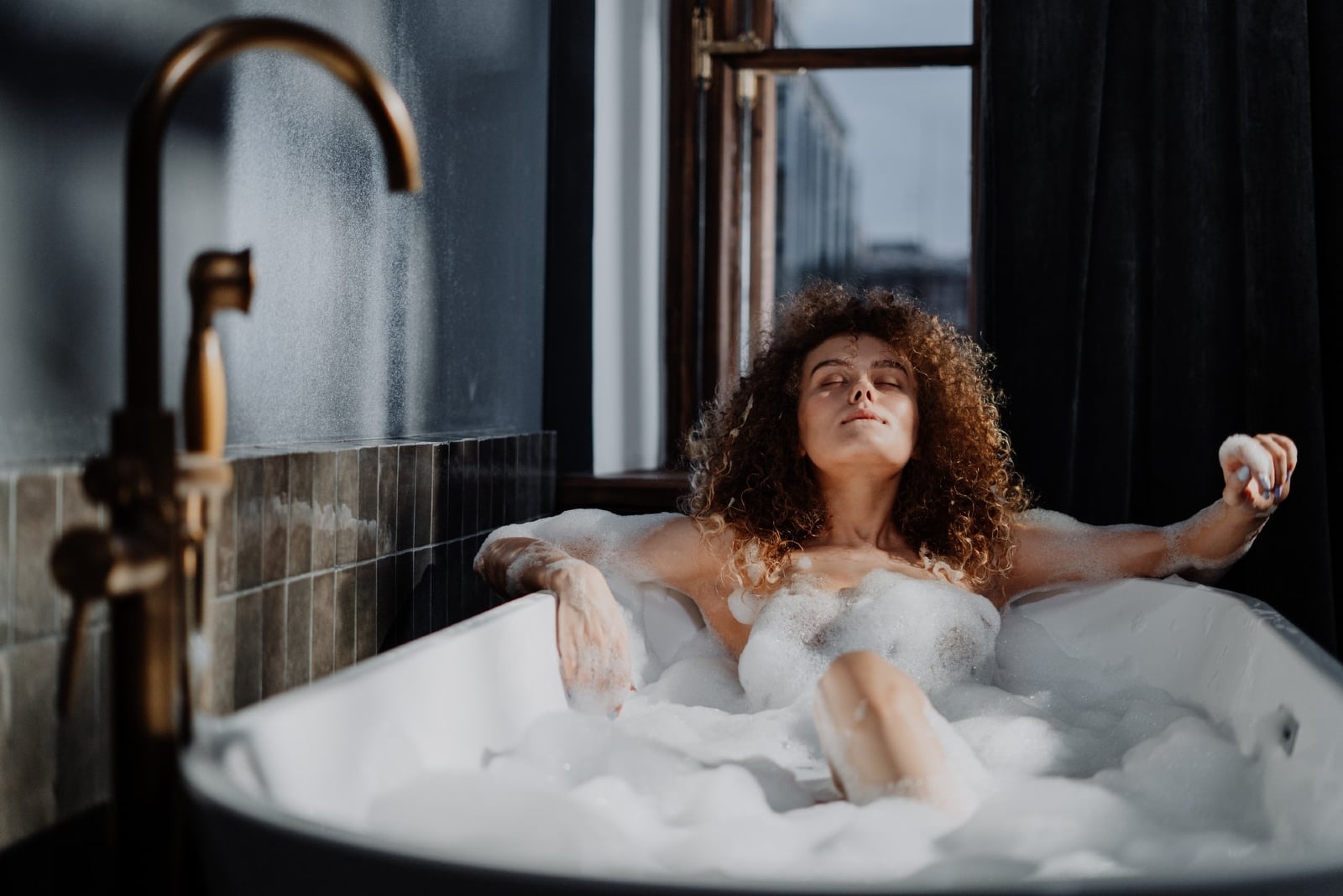 woman with curly hair relaxing in bathtub