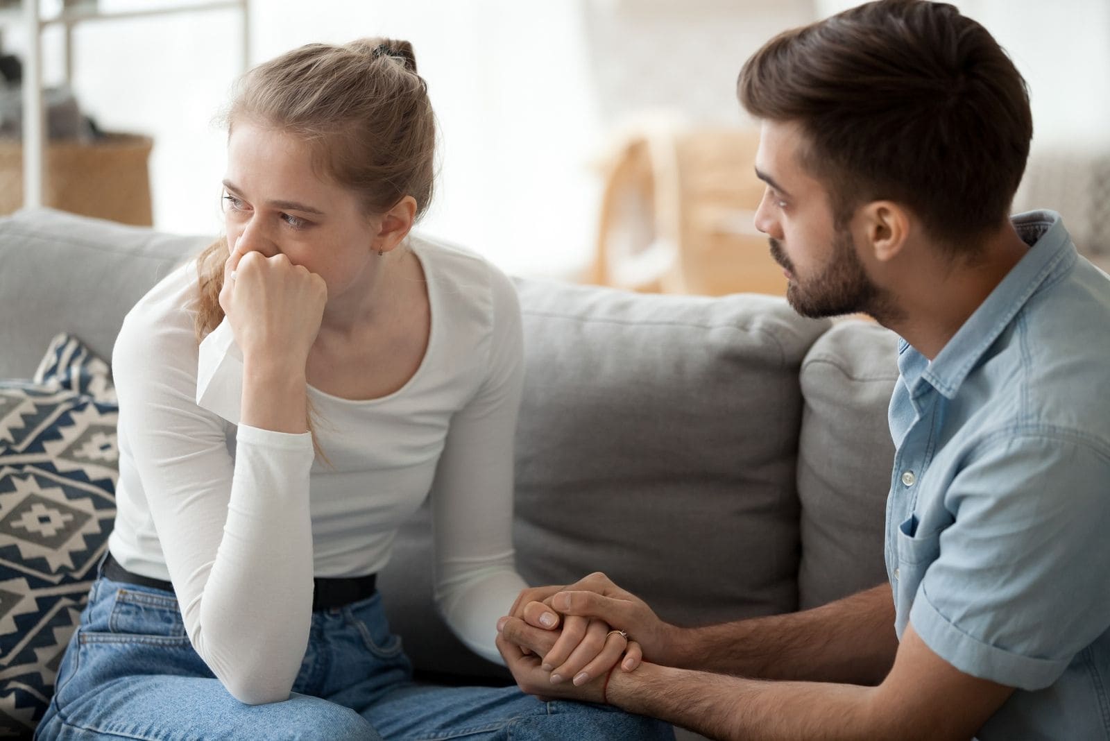 woman sad and crying being consoled by husband sitting in the same sofa inside living room