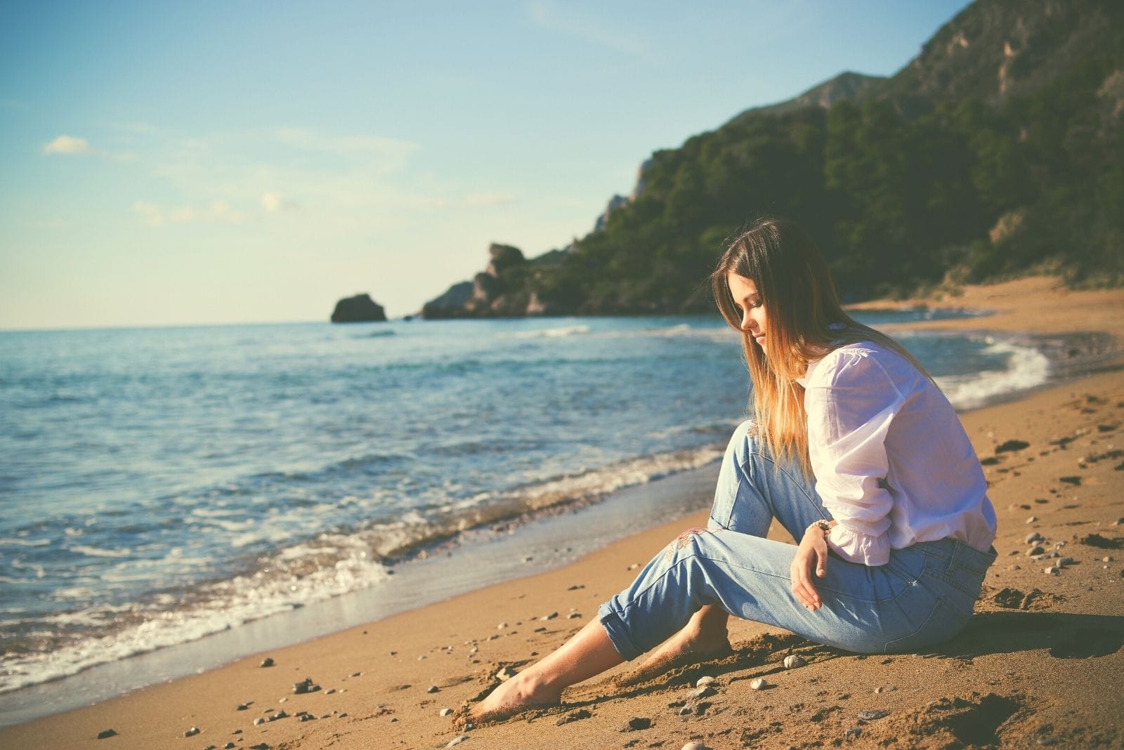 donna seduta da sola in spiaggia mentre pensa lungo l'area della baia