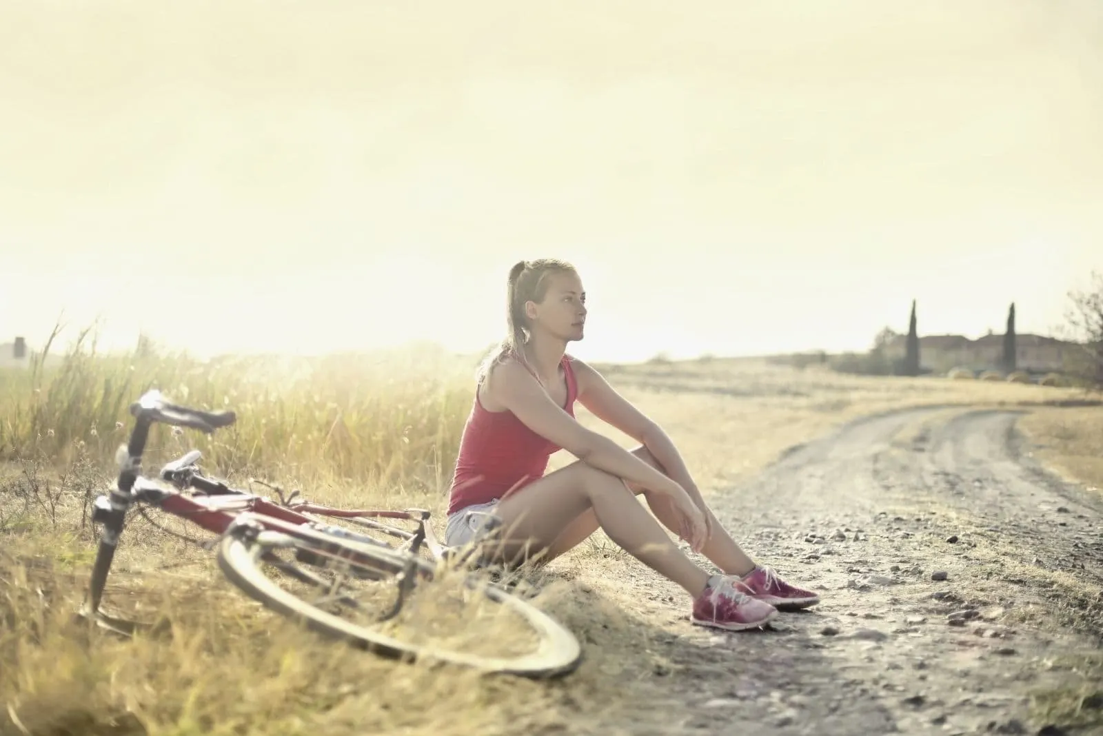 woman sitting by the side of the dirt road with the bike beside her 