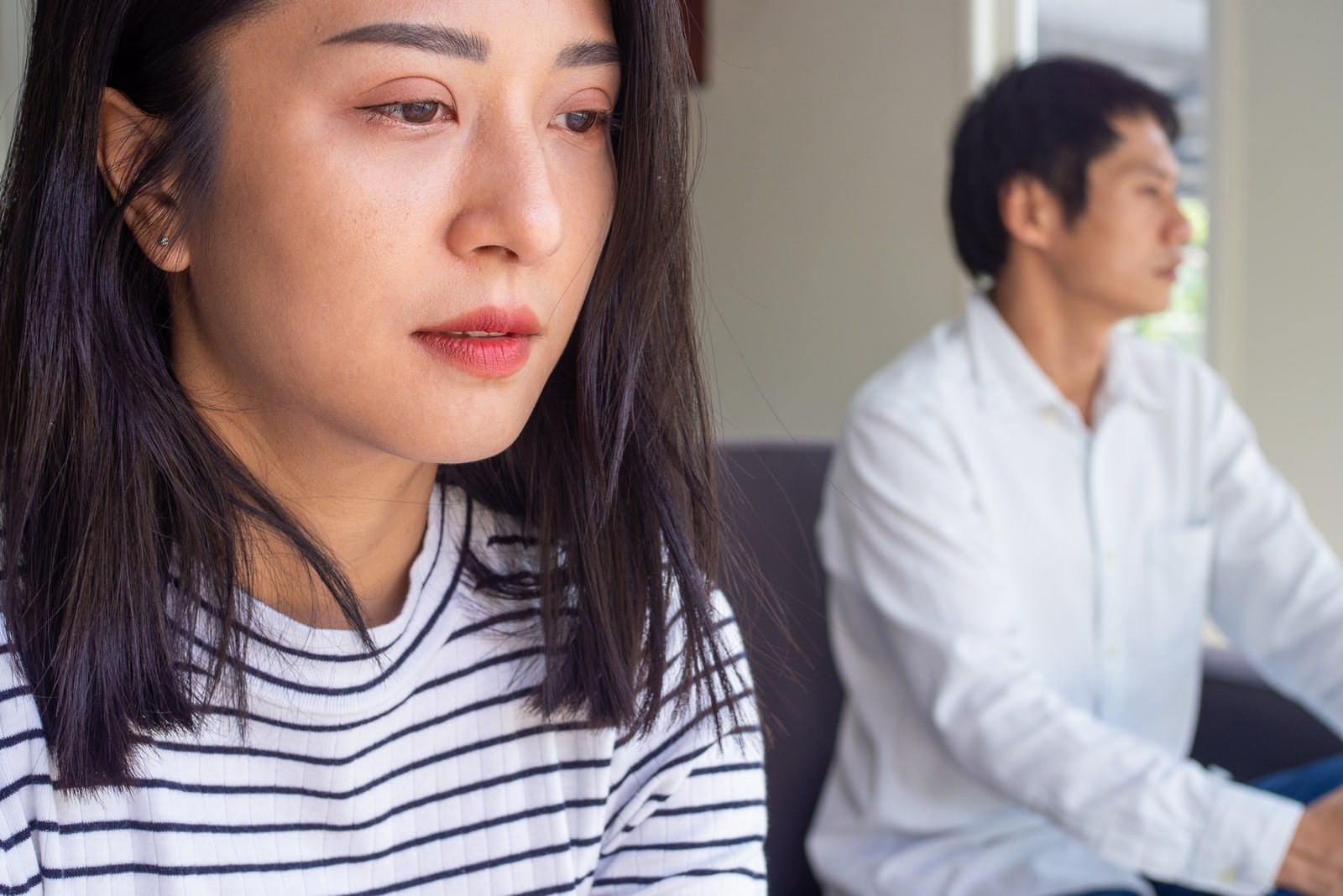 mulher triste com um top às riscas sentada perto de um homem