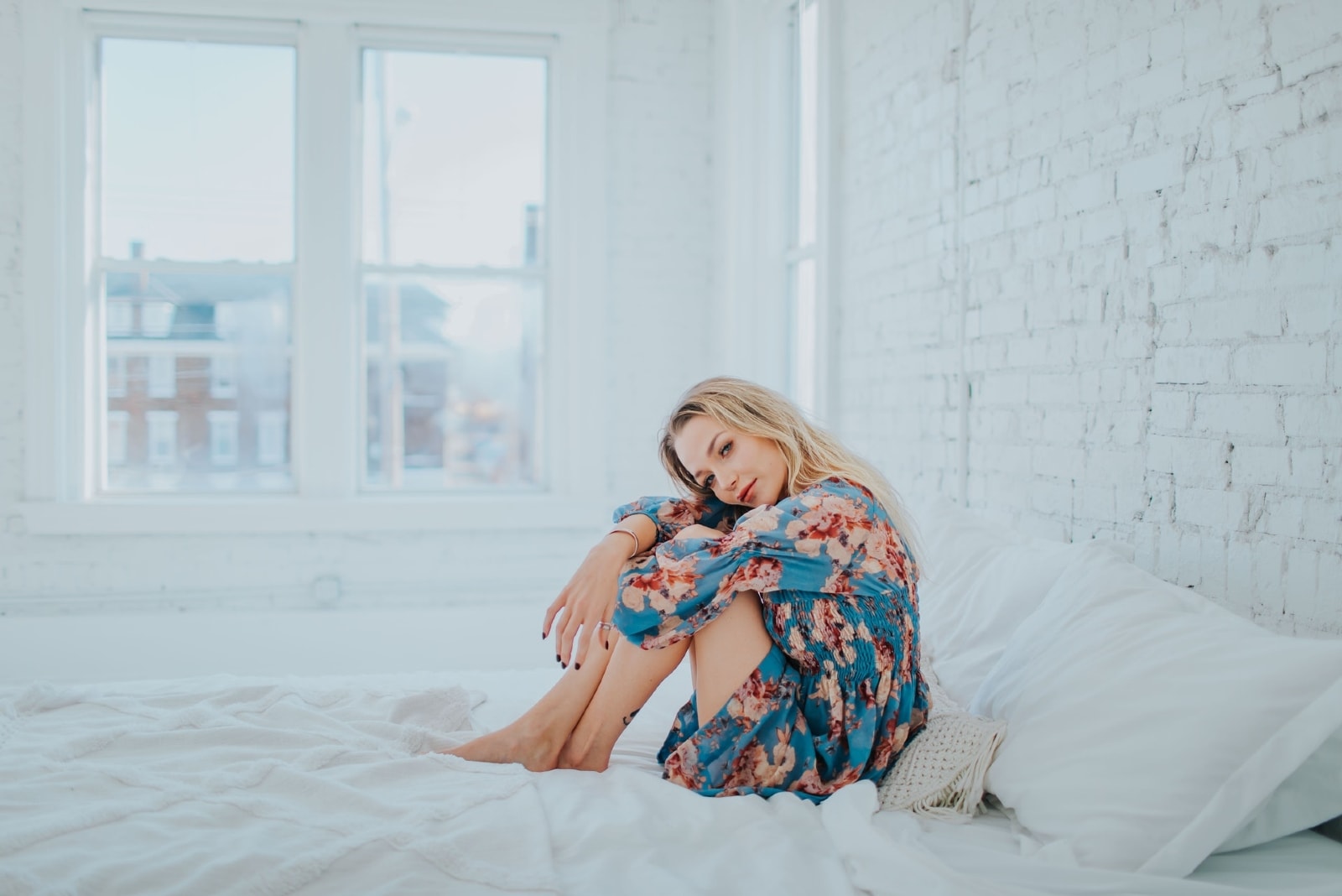 mulher com vestido floral azul sentada na cama