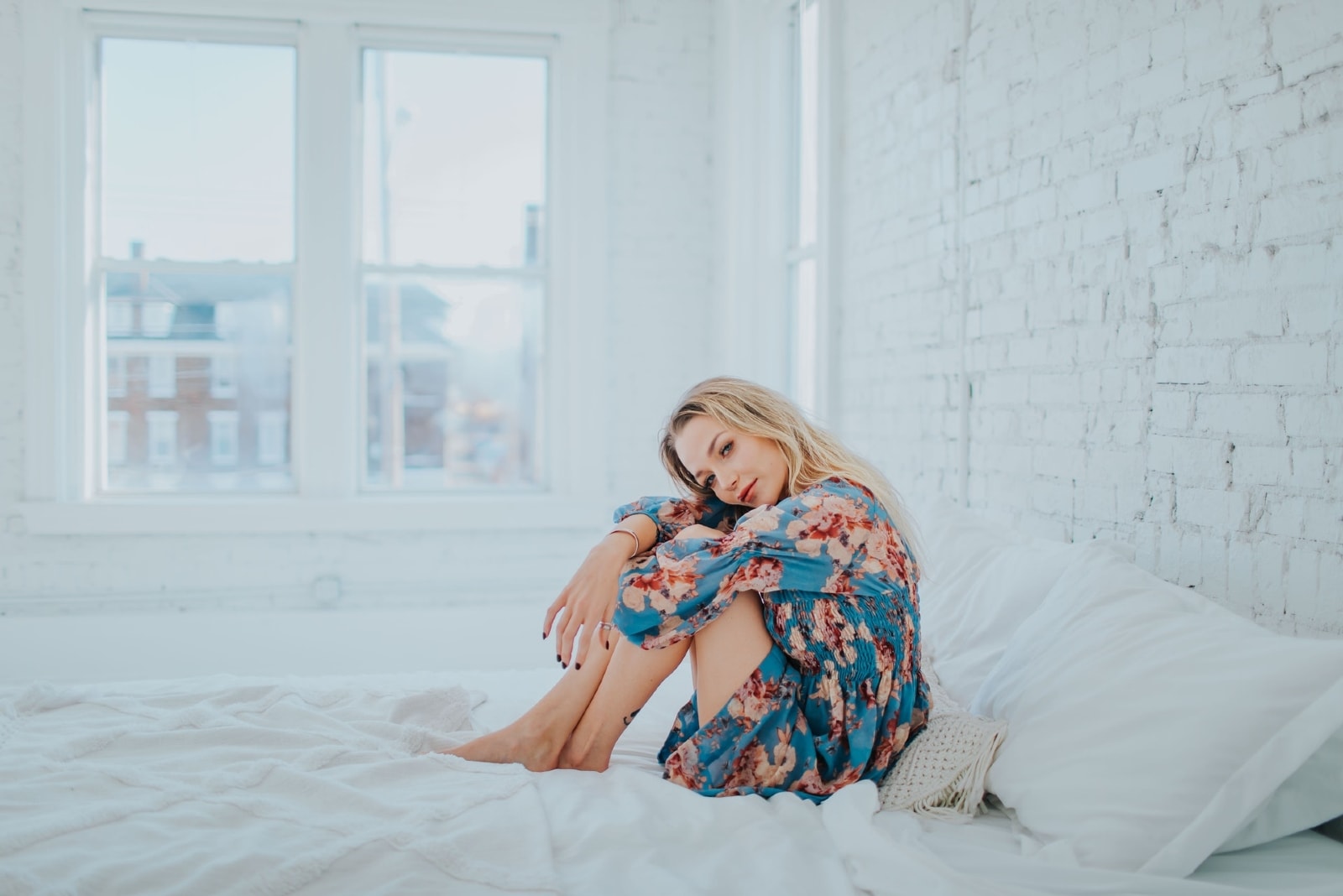 donna bionda in abito floreale seduta sul letto