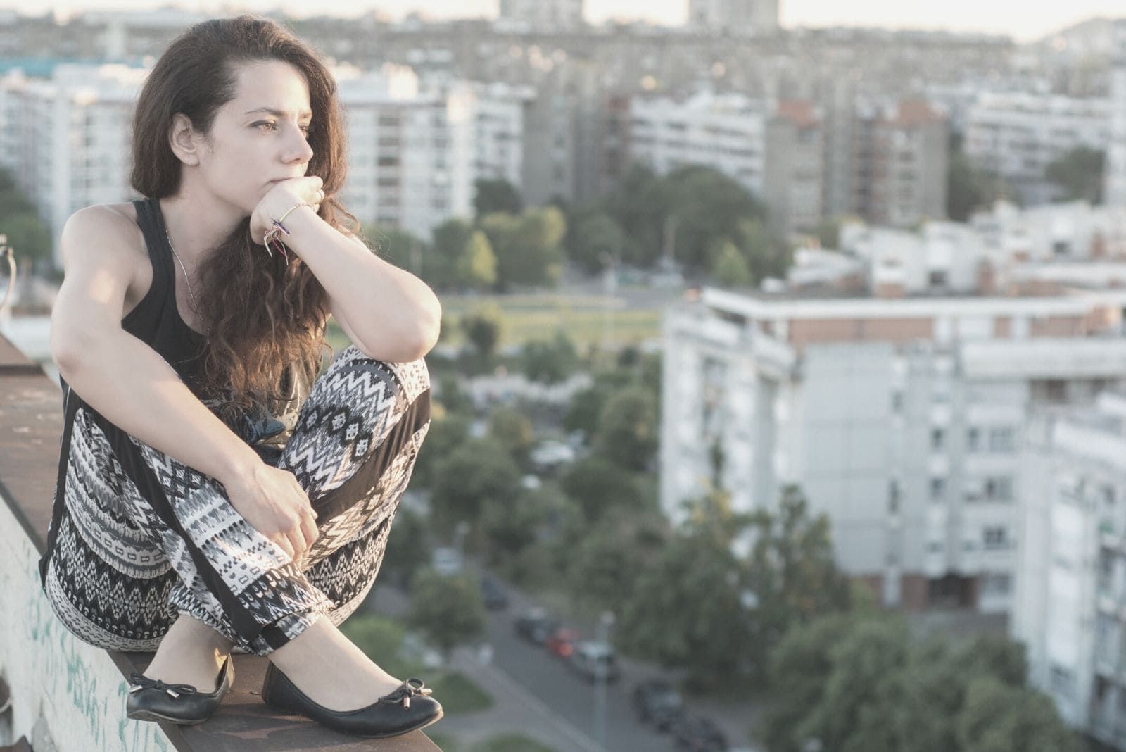 woman sitting on the ledge on top of the building thinking deeply