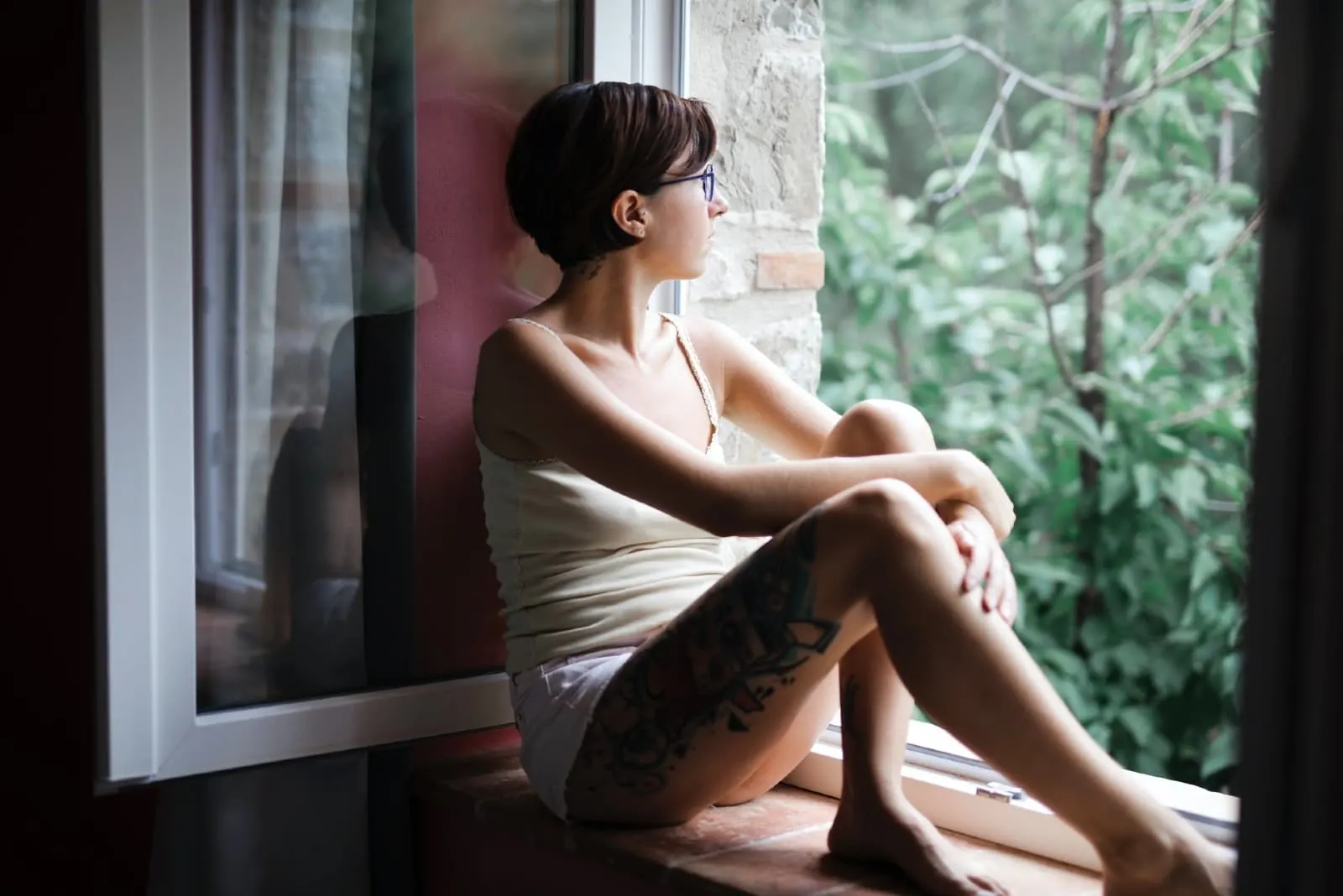woman in white top sitting on window pane looking outside