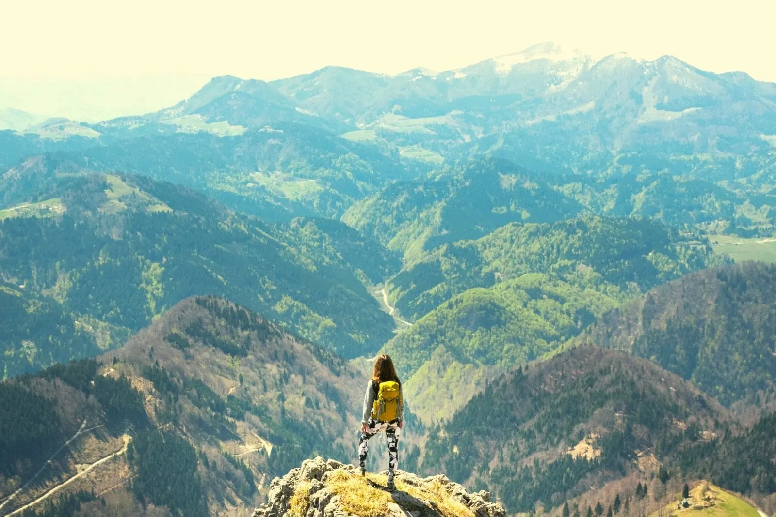 woman standing at the mountain top looking over the mountain ranges in very distant view