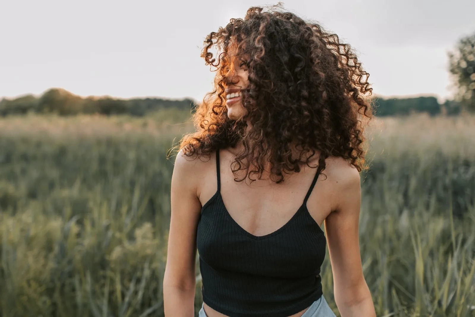 woman with curly hair standing in the field smiling