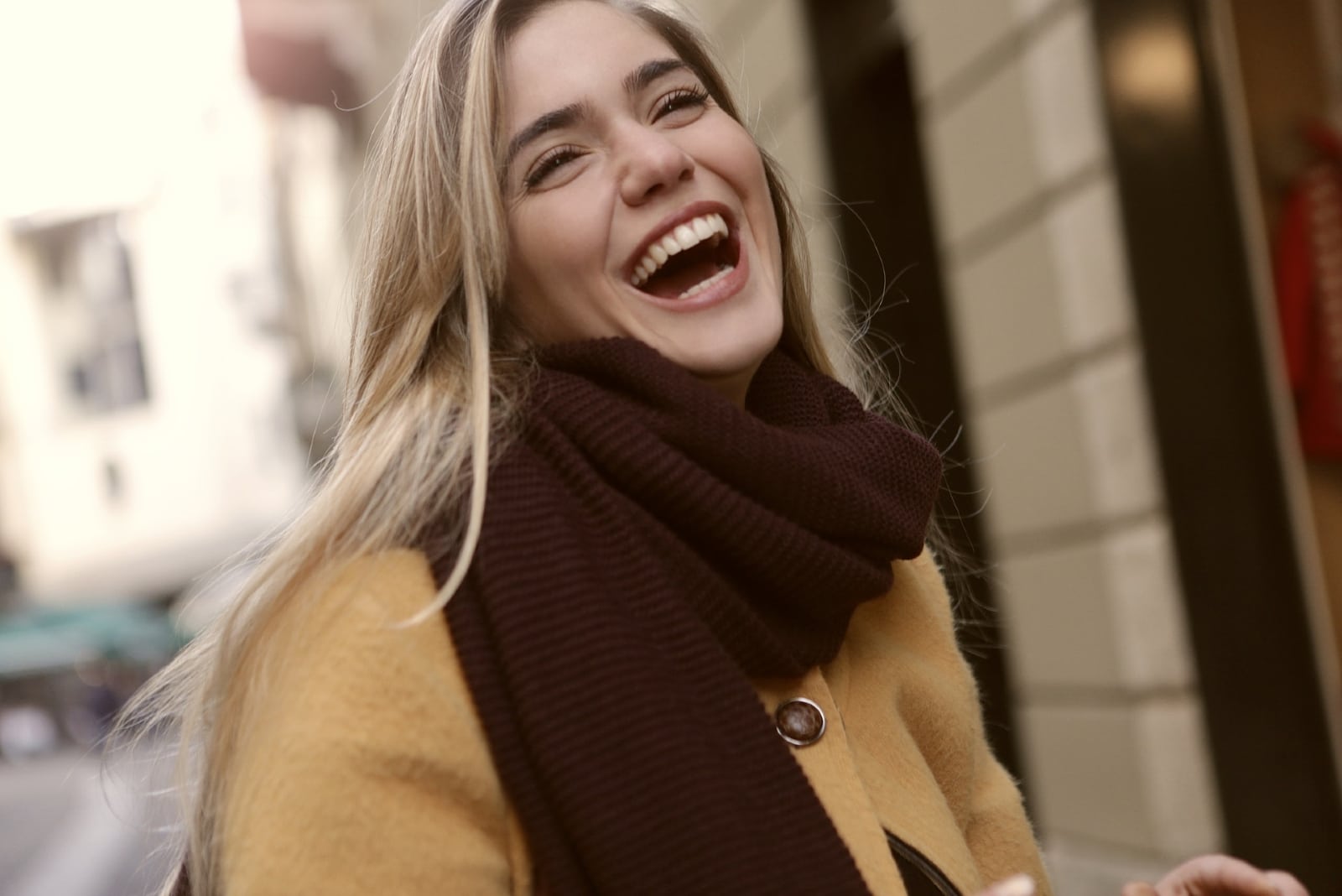 woman with brown scarf laughing while standing near building