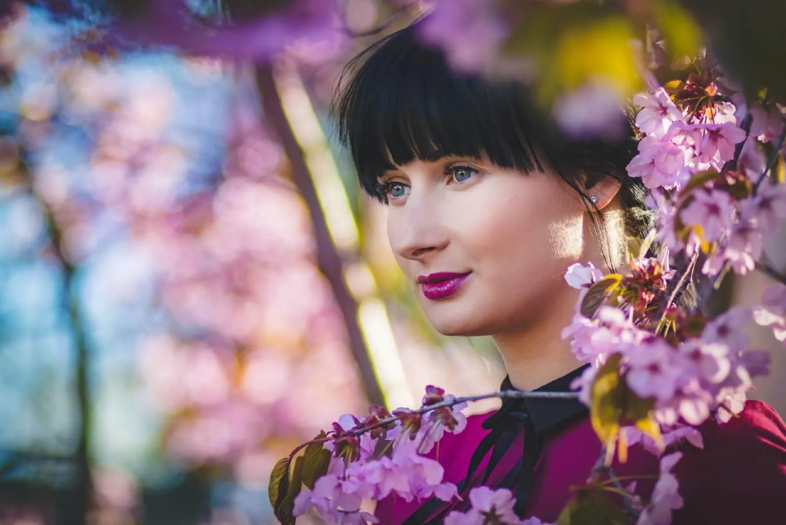 woman with purple lipstick standing near pink flowers