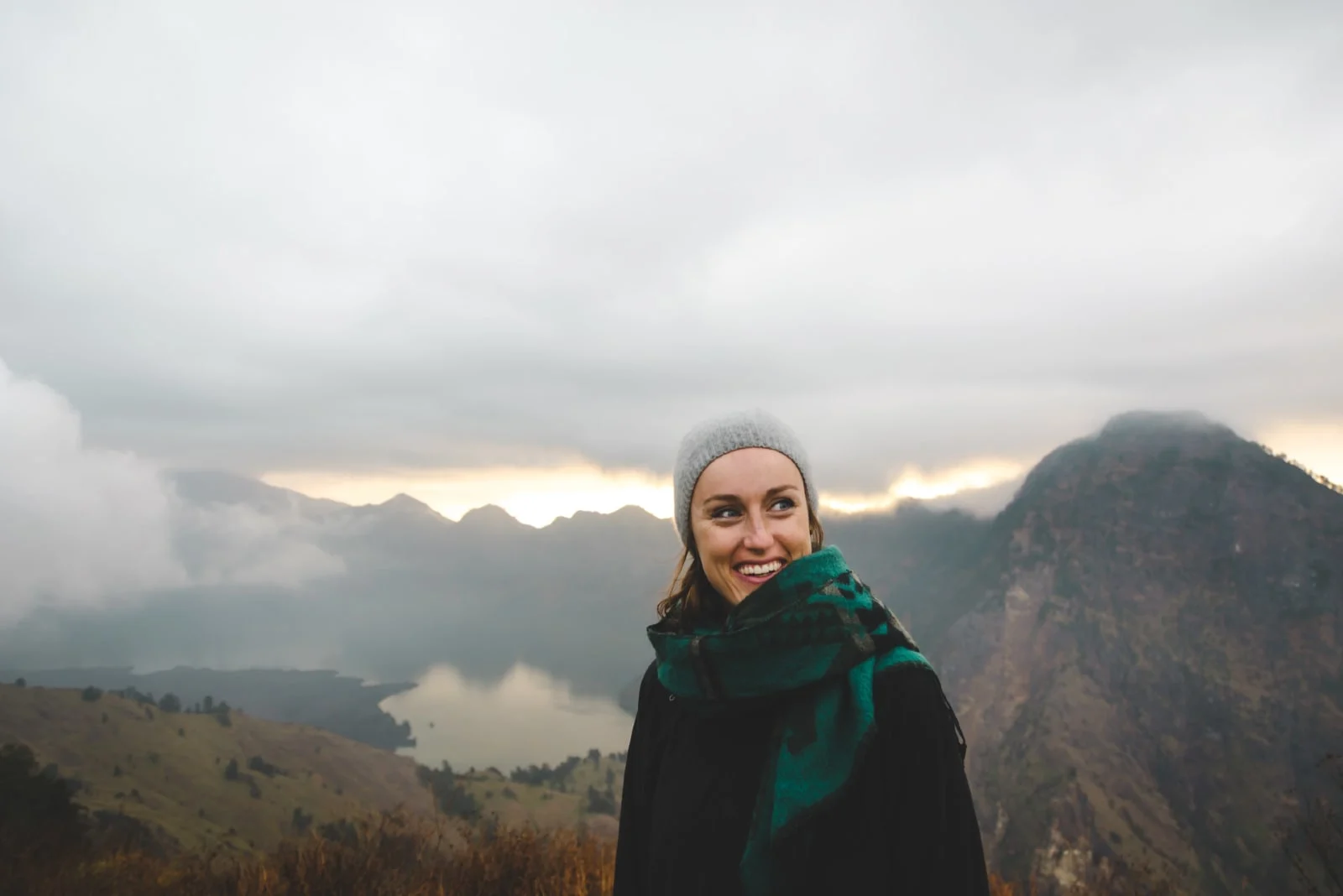 woman with green scarf smiling while standing near mountain