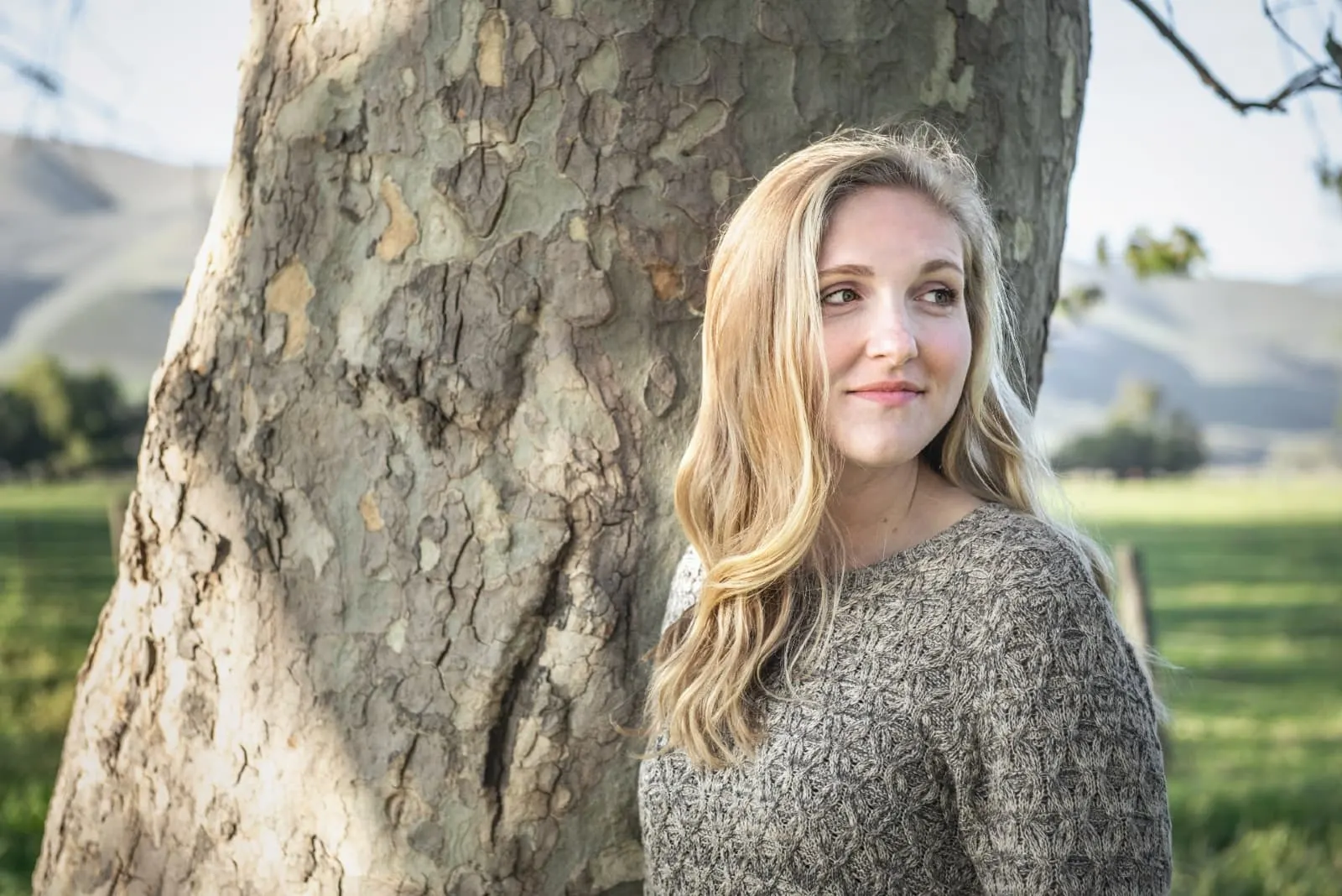 blonde woman in gray sweater standing near tree