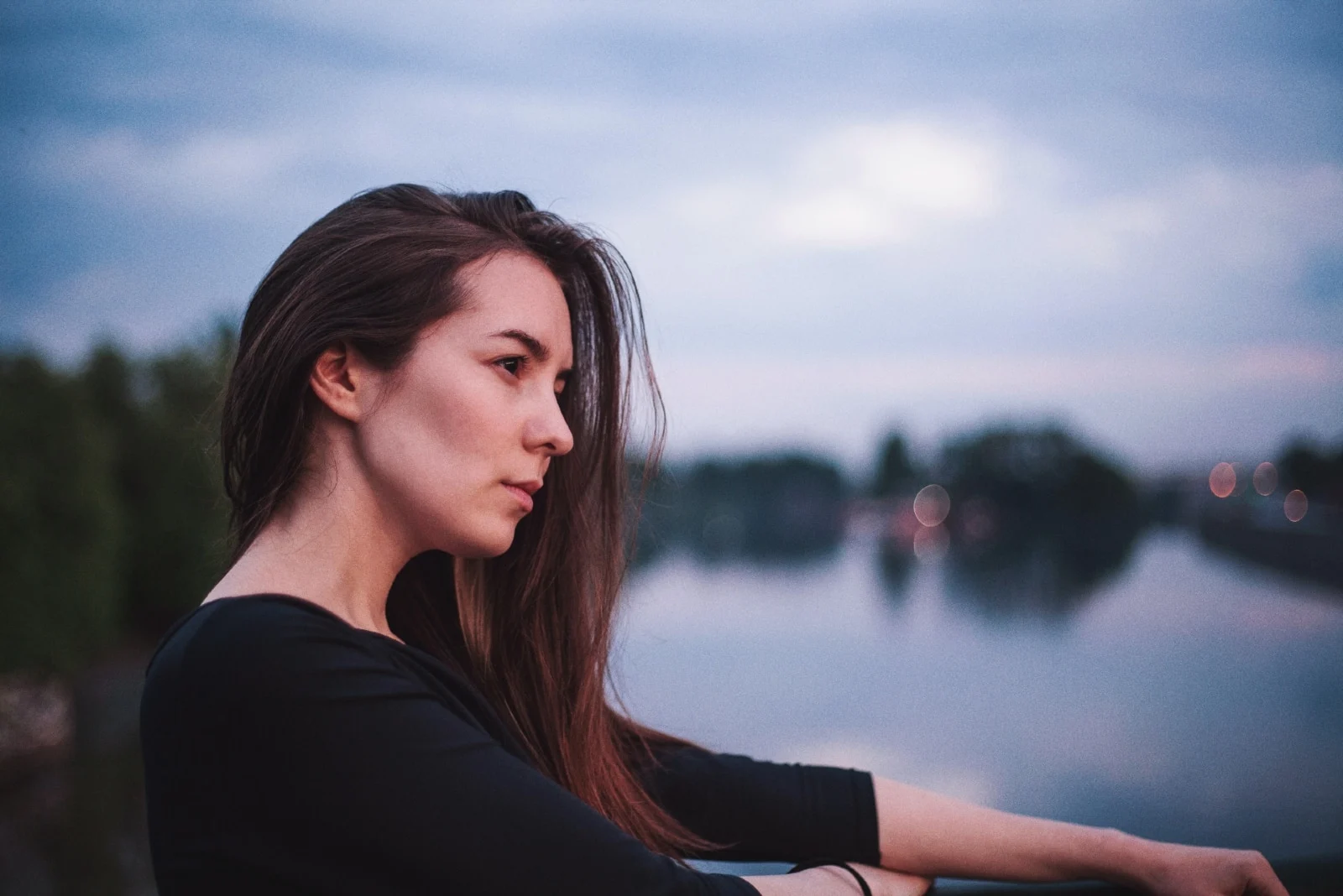 pensive woman in black top standing near water
