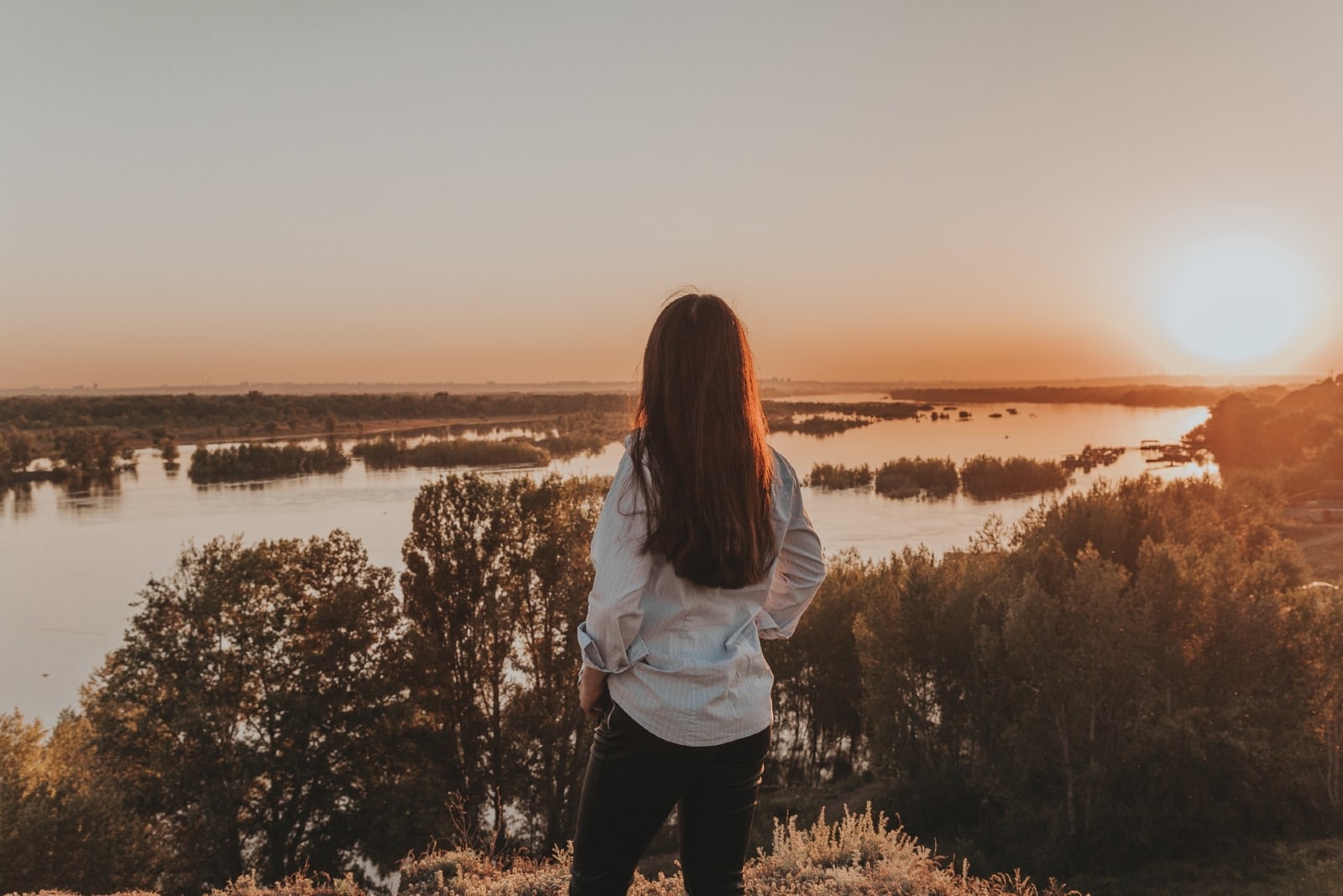 woman standing on hill looking at lake