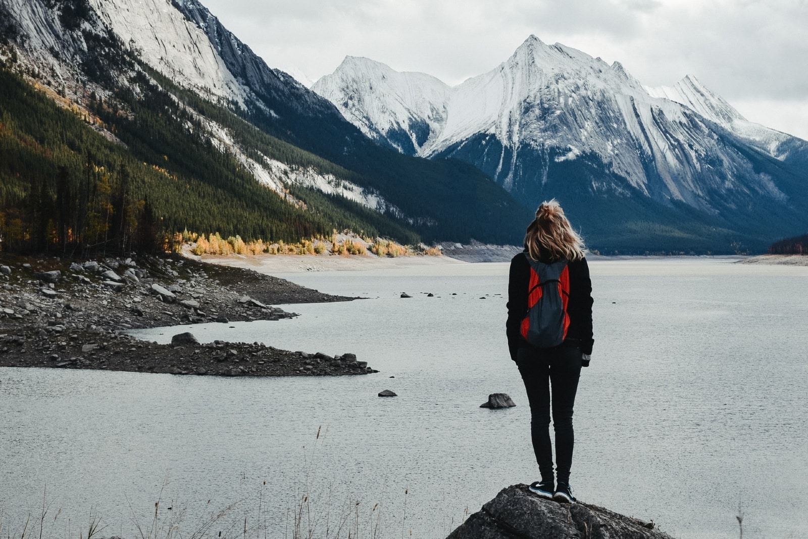 donna con zaino in piedi su una roccia che guarda il lago