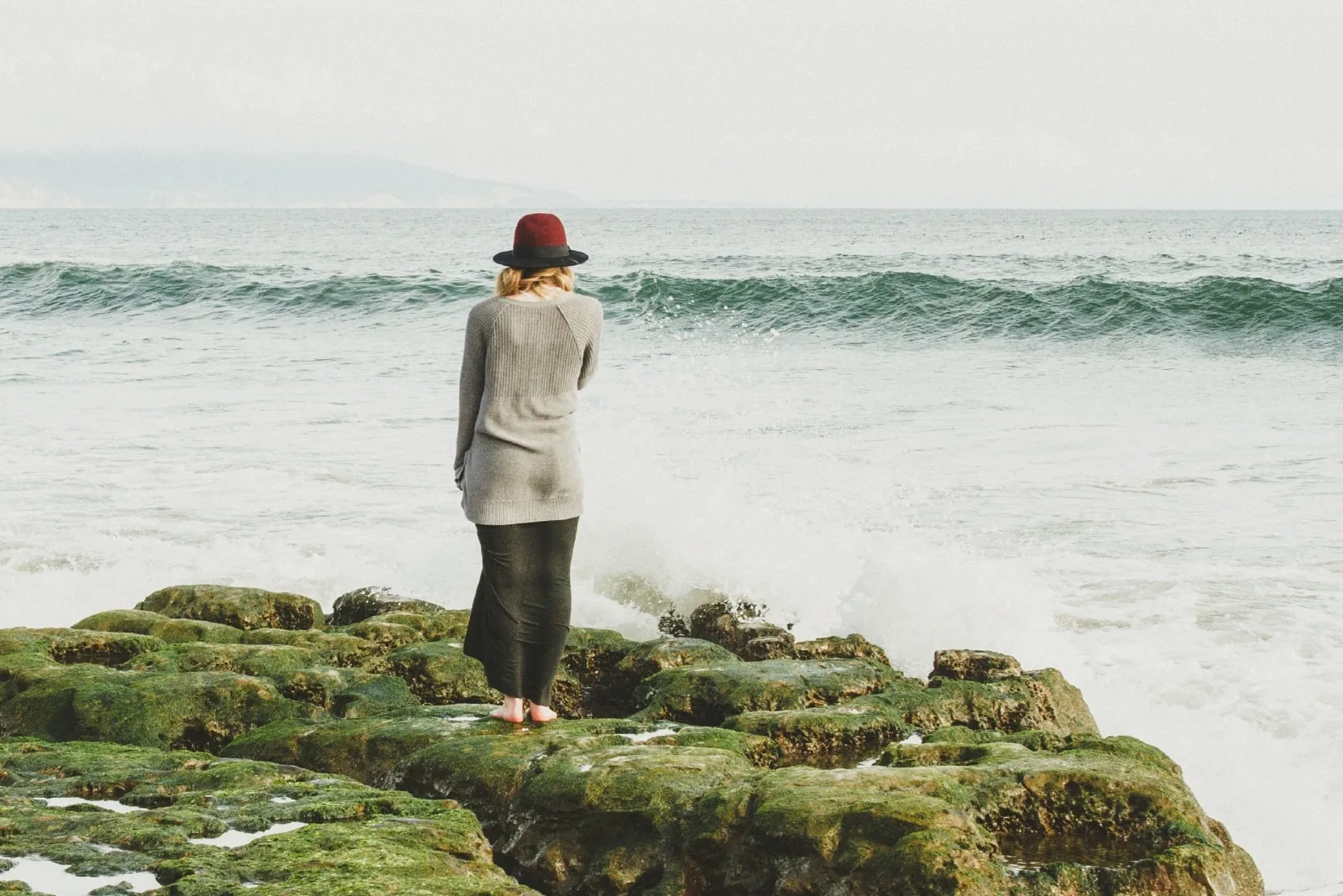 woman with hat standing on rock looking at sea