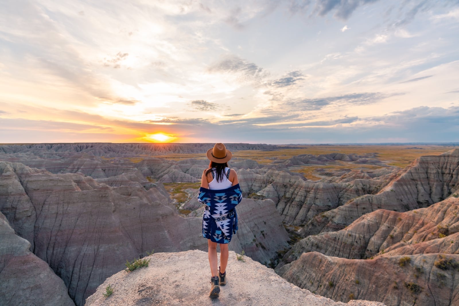 donna con cappello in piedi sulla roccia durante il tramonto