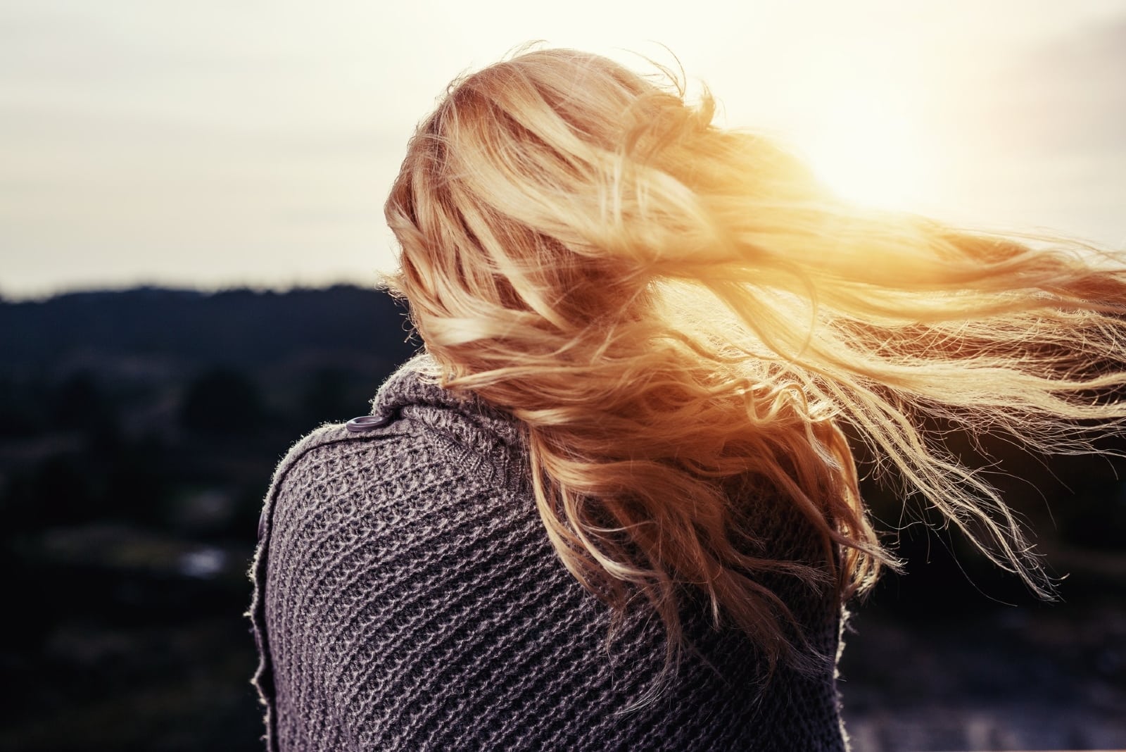 mujer en suéter gris de pie al aire libre durante la puesta de sol