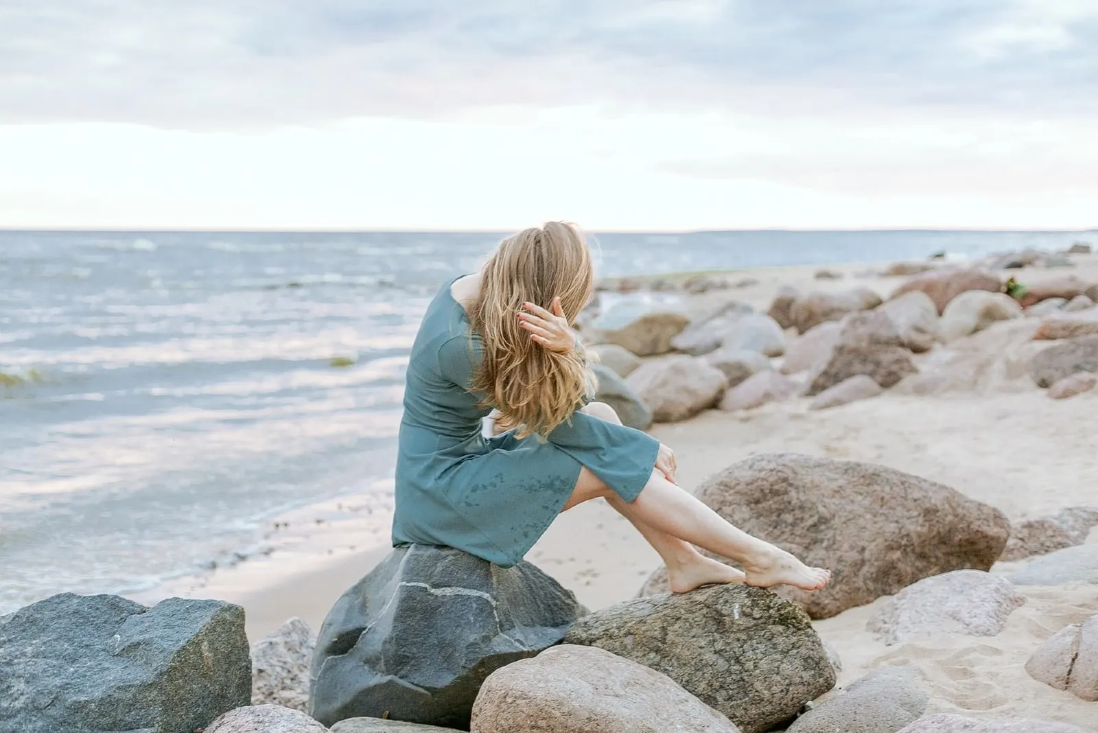 woman touching her hair while sitting on rock