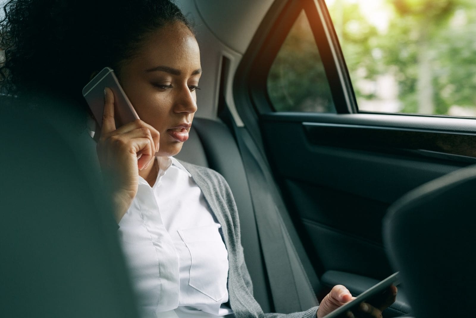 mulher a utilizar o telemóvel para fazer chamadas e a navegar no outro, dentro do carro, sentada no banco de trás