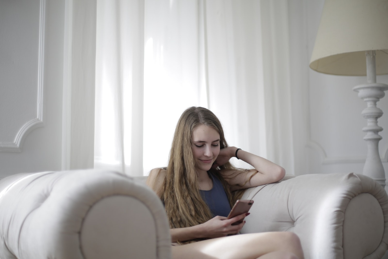 woman using smartphone while sitting in white armchair