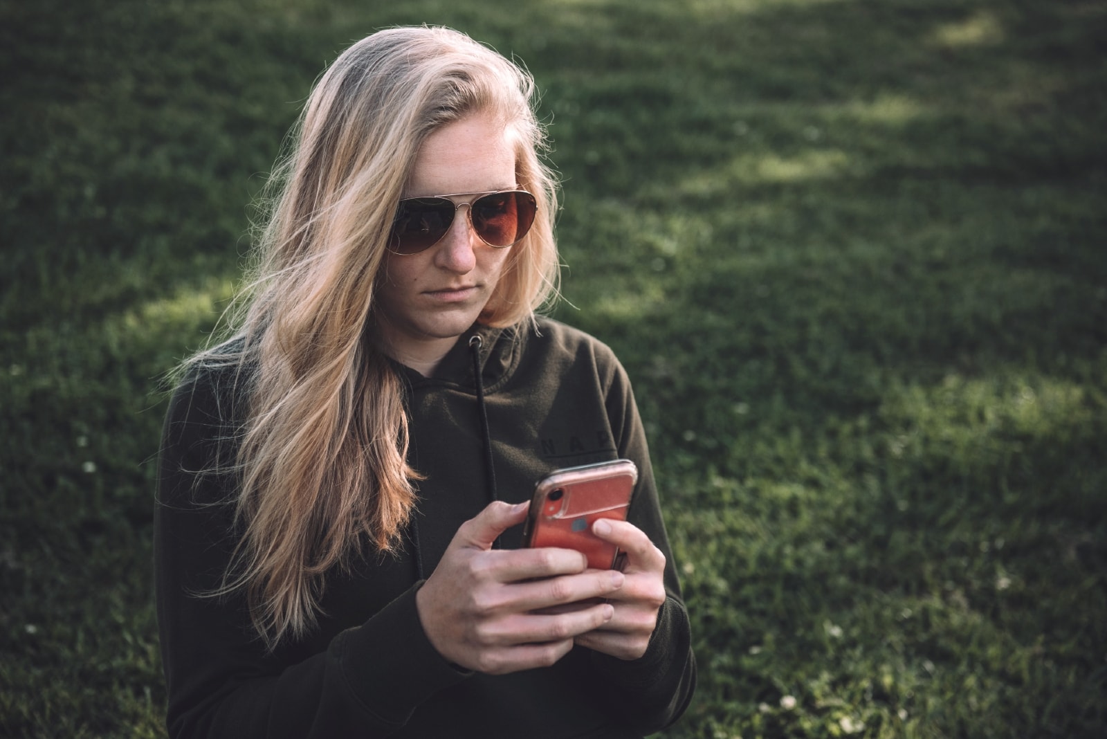 mulher loira com óculos de sol a utilizar um smartphone no exterior