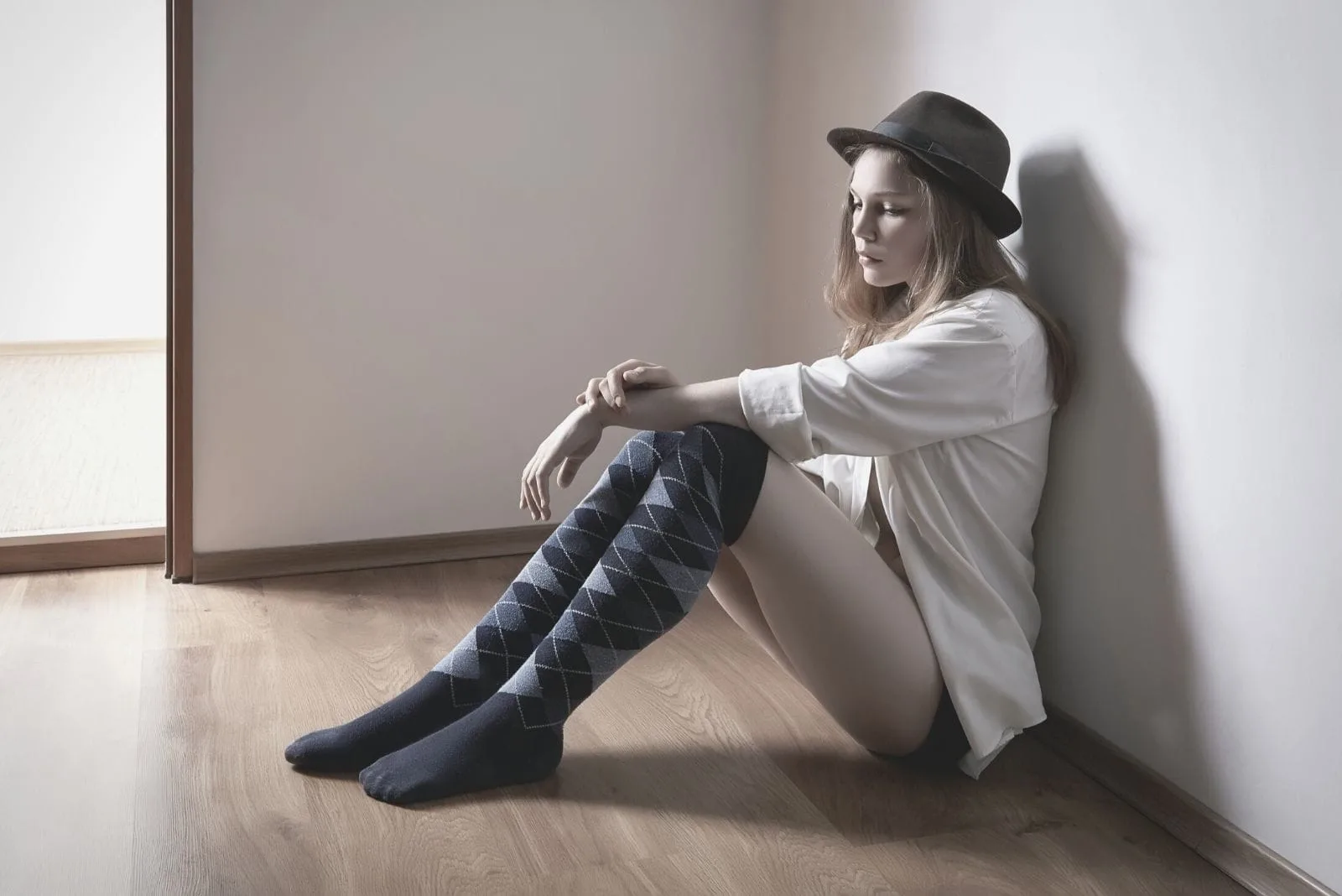 woman with a hat sitting on the floor inside the room looking sad