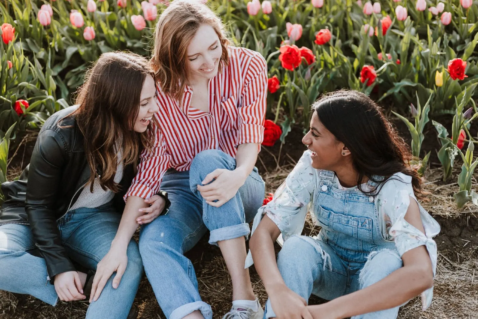 three women sitting near tulips field smiling