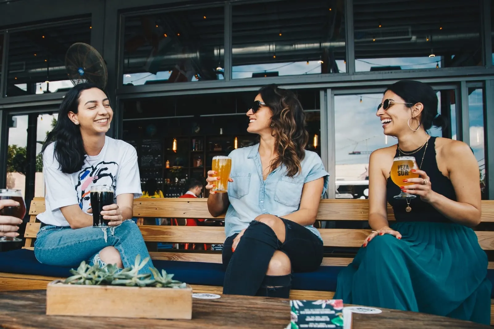 three women holding glasses of beer while sitting on bench