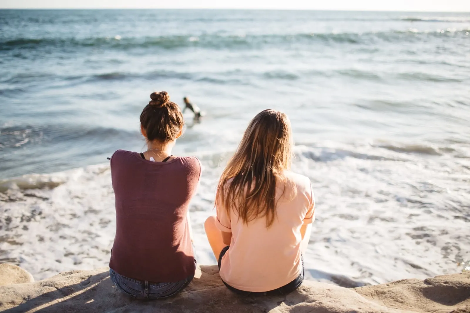 two women sitting on cliff looking at sea