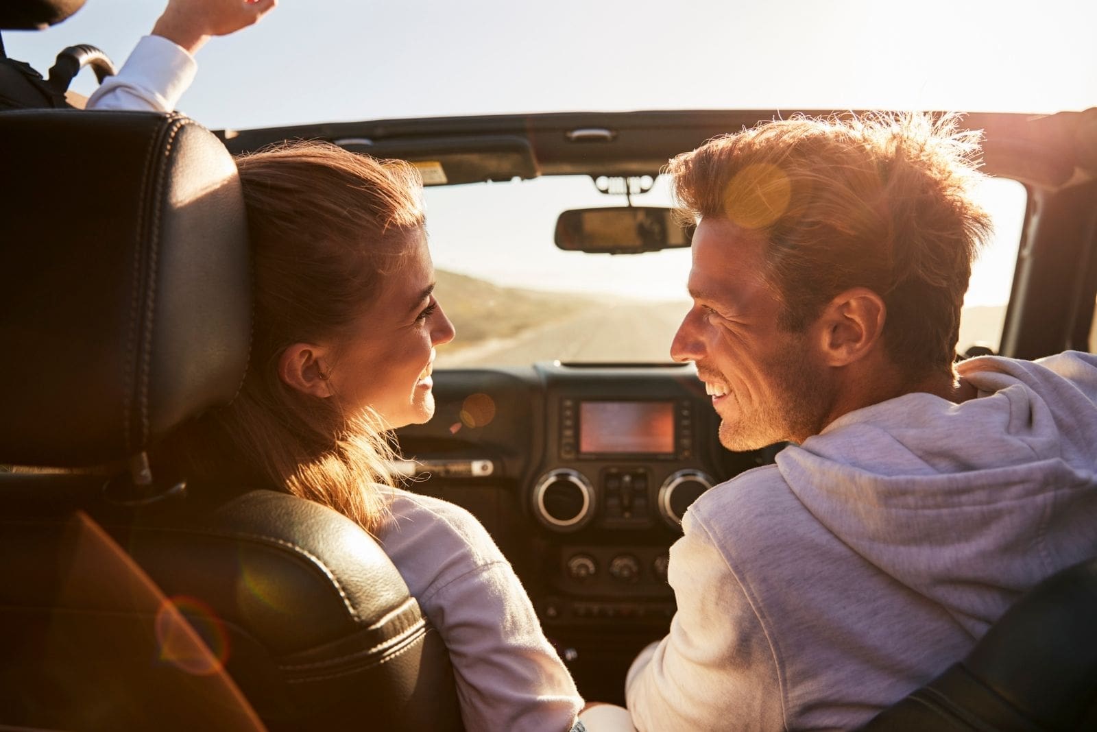 young couple glancing at each other while driving on open top car