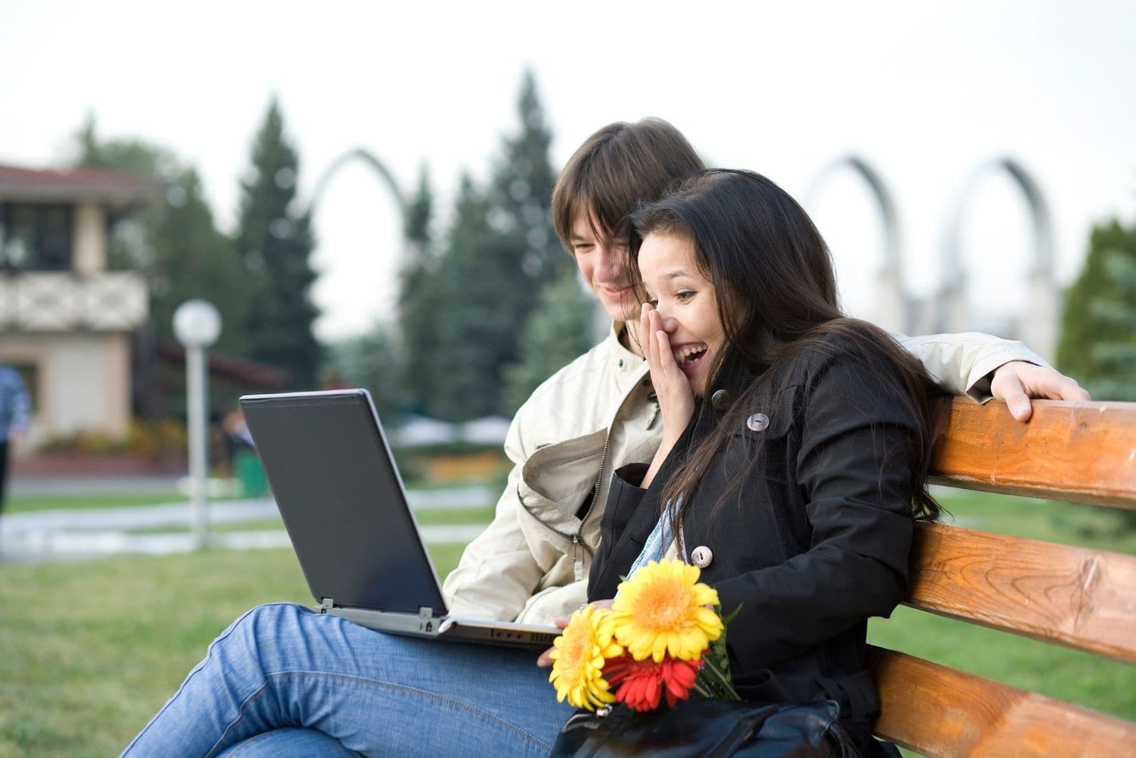 young couple watching movie on laptop while sitting on the bench outdoors