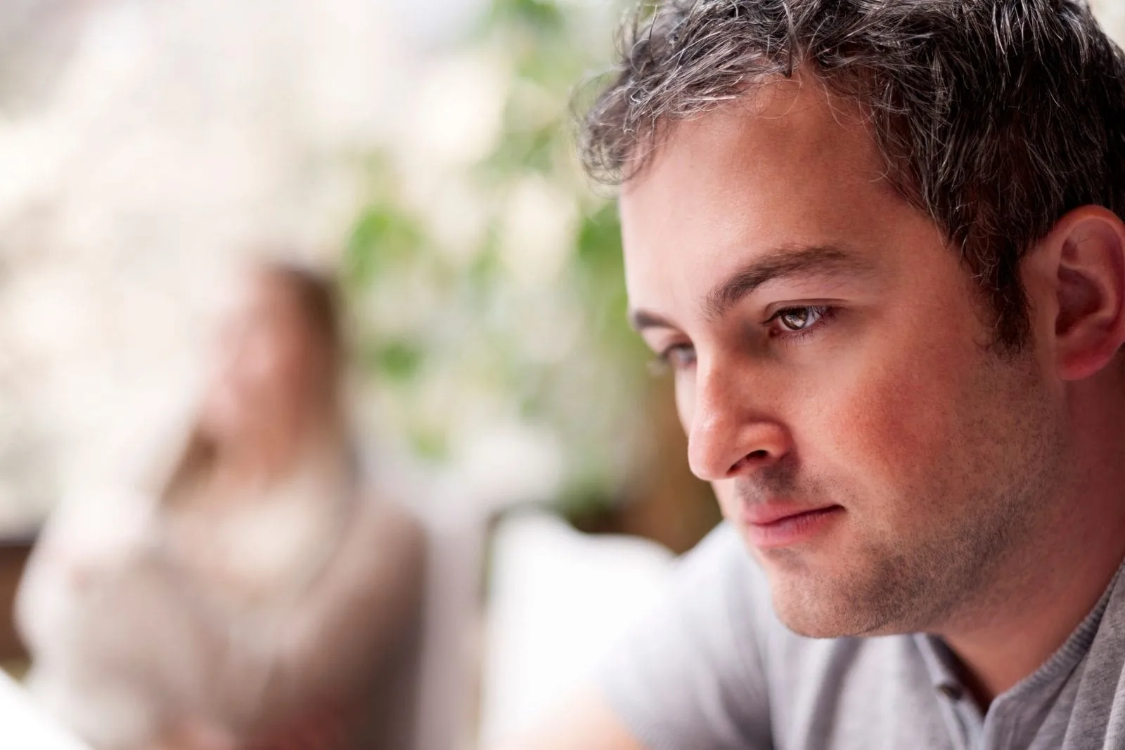 young pensive man focus on his face with blurry image of a woman apart from him
