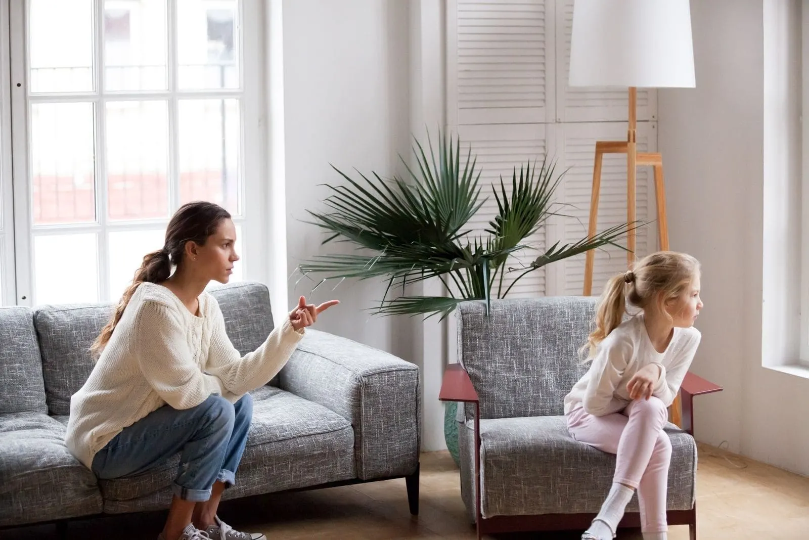 young strict mother scolding her stubborn child sitting inside living room
