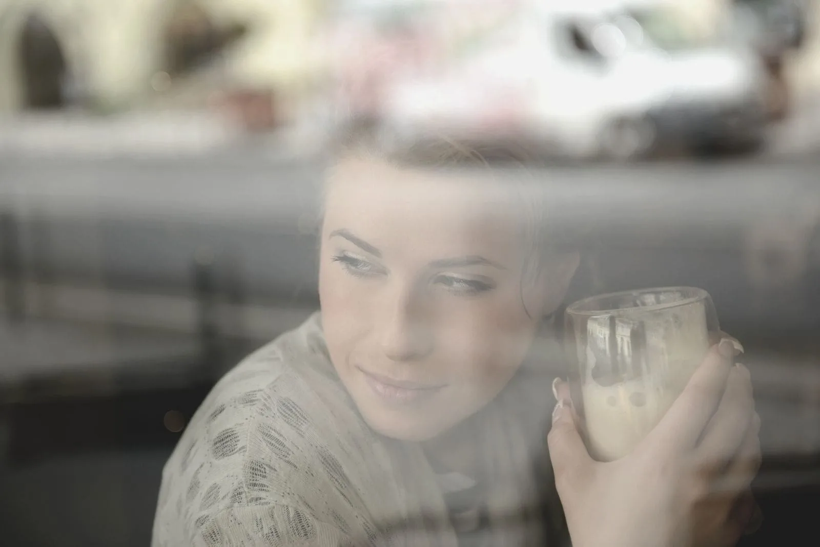 young woman holding a glass of frappe behind window thinking